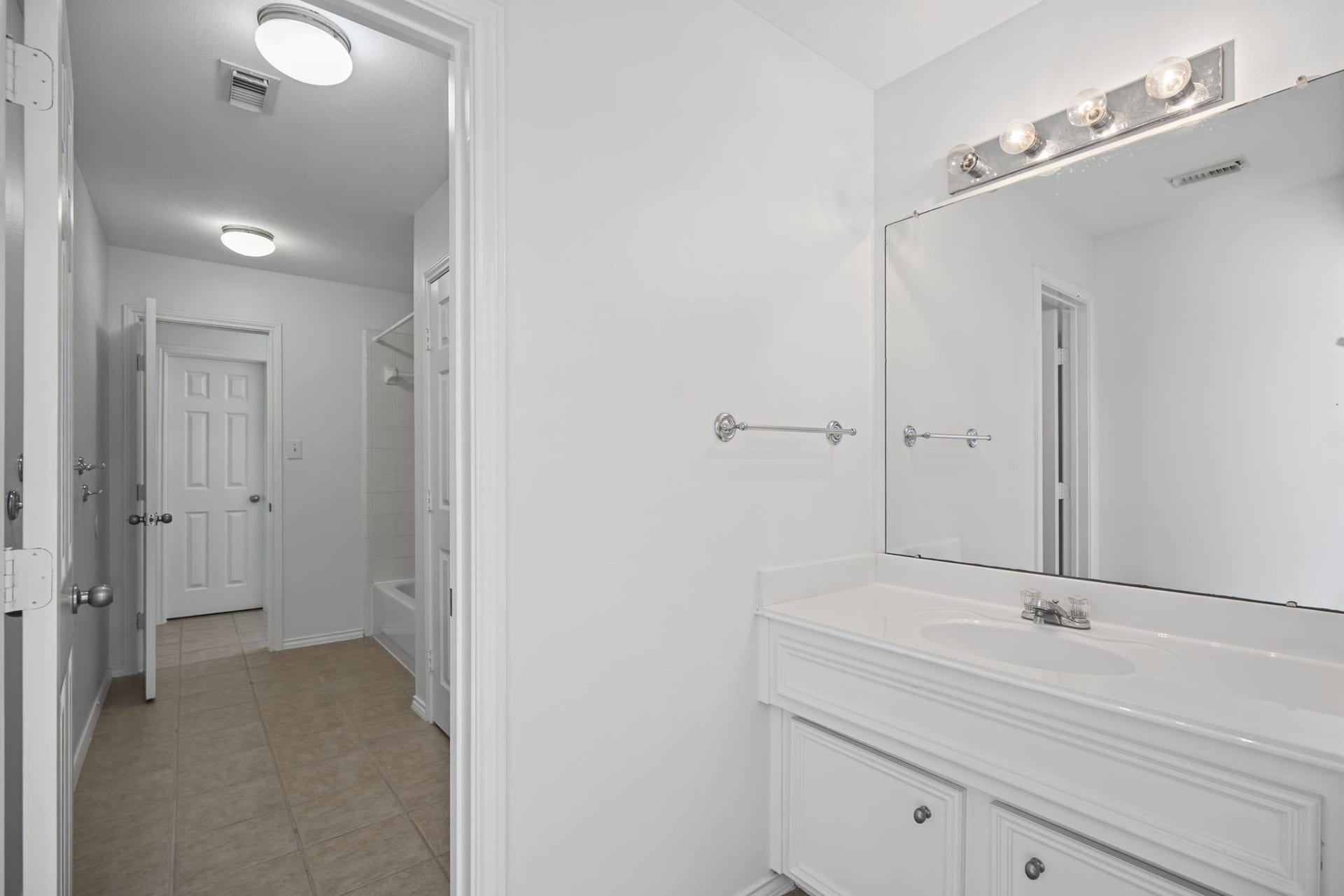 The upstairs bathroom presents a white vanity with cabinet storage, a broad mirror, and coordinated overhead lighting.