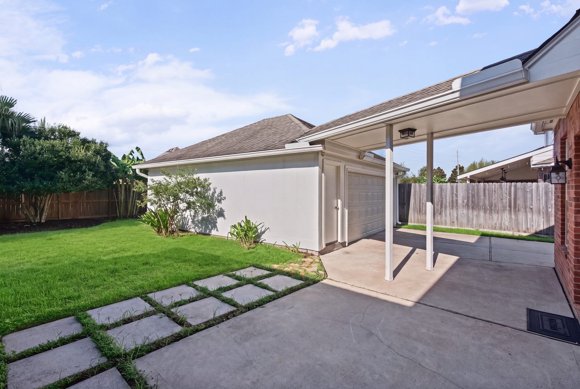 Step outdoors to a paved patio and covered passage linking the house and garage, with stepping stones extending into the lawn. Sellers installed a smart irrigation device (rachio 3) for sprinkler controllers.