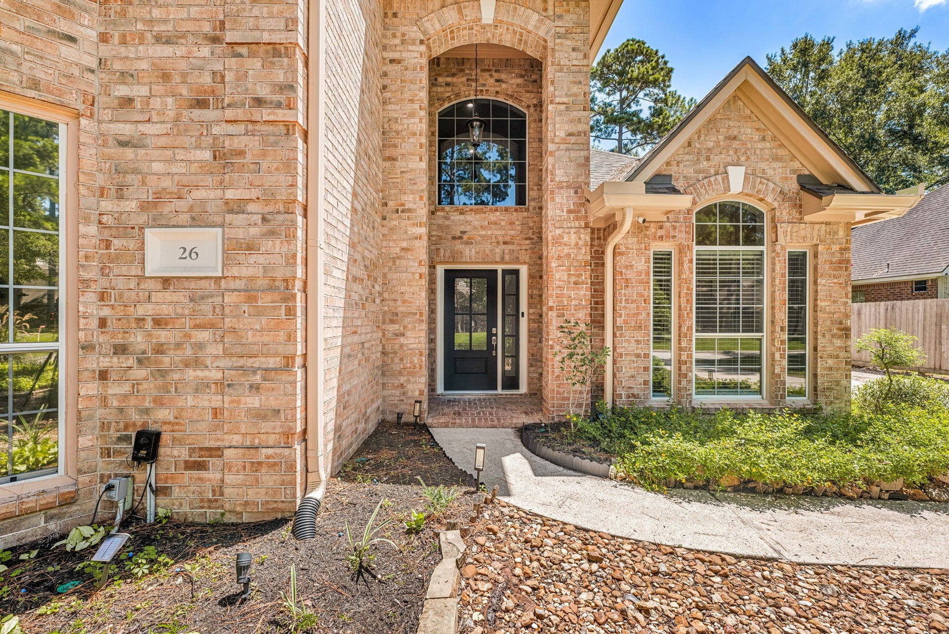 Stunning brick exterior with elegant arched windows and a welcoming entrance, set amidst lush landscaping.