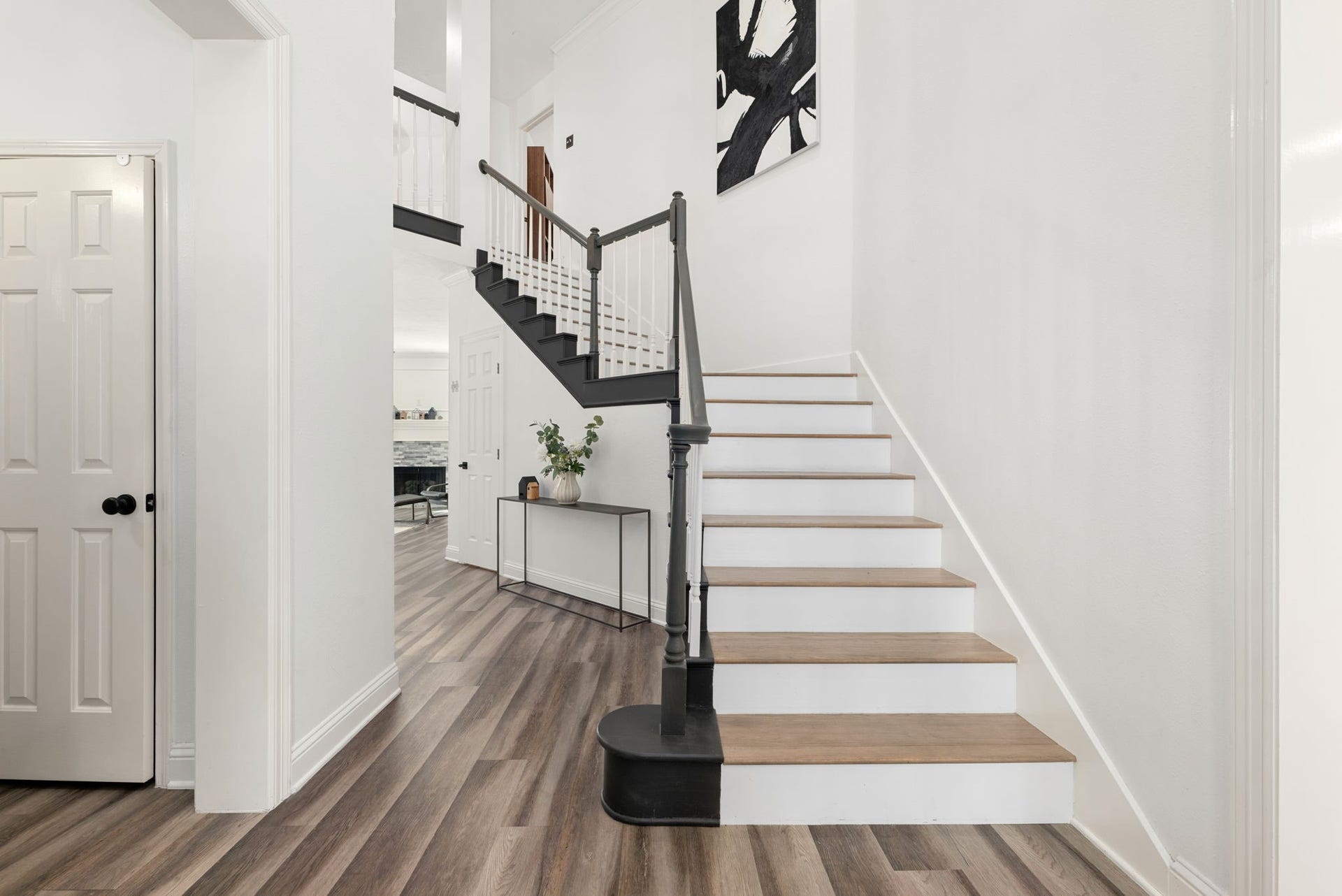 Elegant staircase with a modern black railing and light wood steps, set against pristine white walls. The open layout and sleek flooring enhance the contemporary feel, leading seamlessly into the living area.