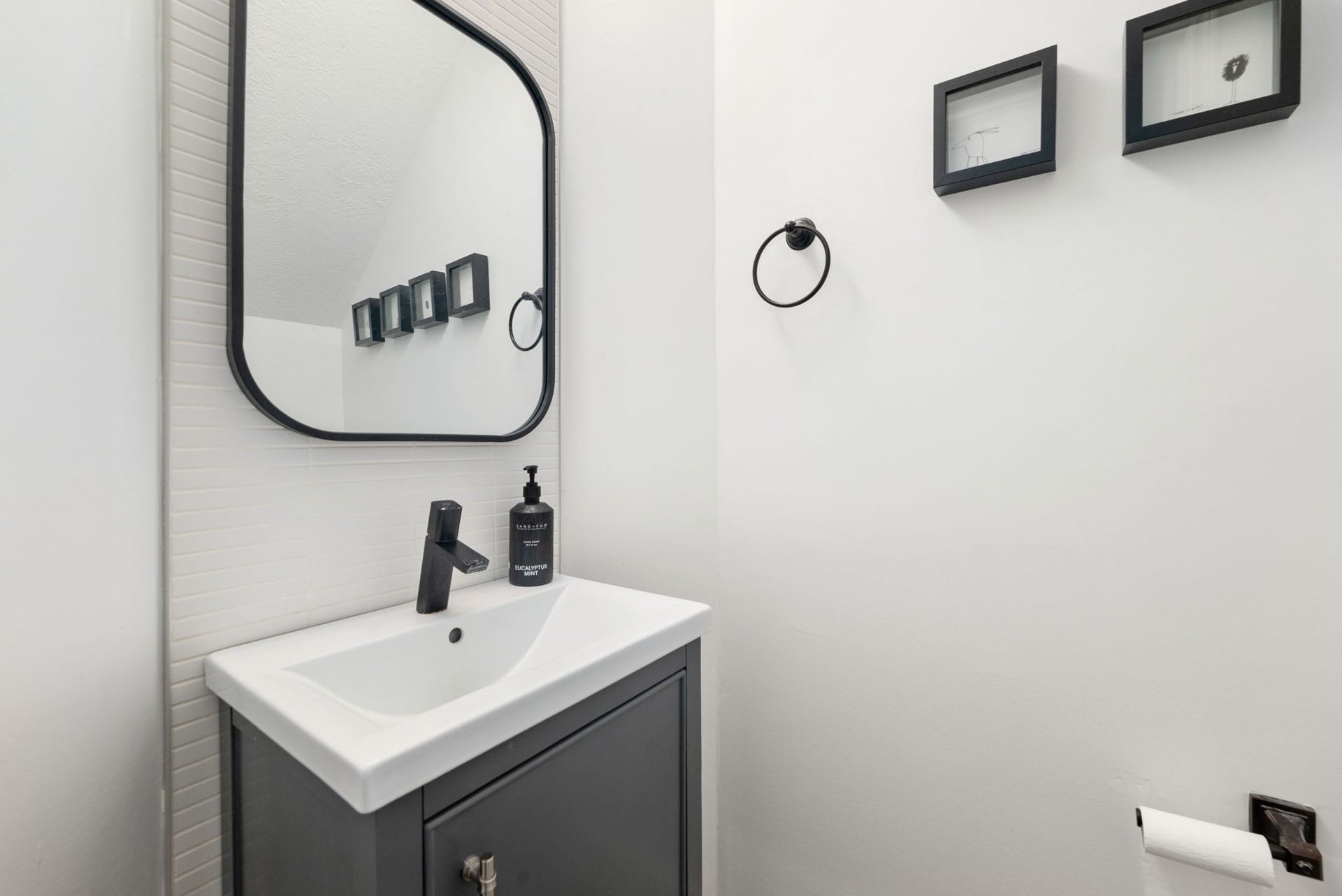 Modern half-bath with sleek fixtures, featuring a stylish black vanity and framed mirror for a contemporary touch.
