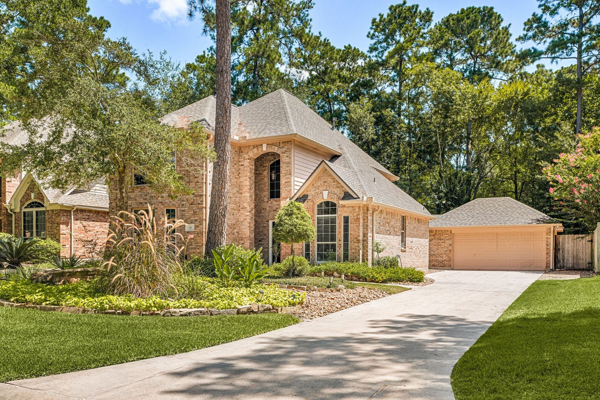 Stunning brick home nestled among mature trees, featuring a spacious driveway leading to a detached garage and beautifully landscaped front yard.