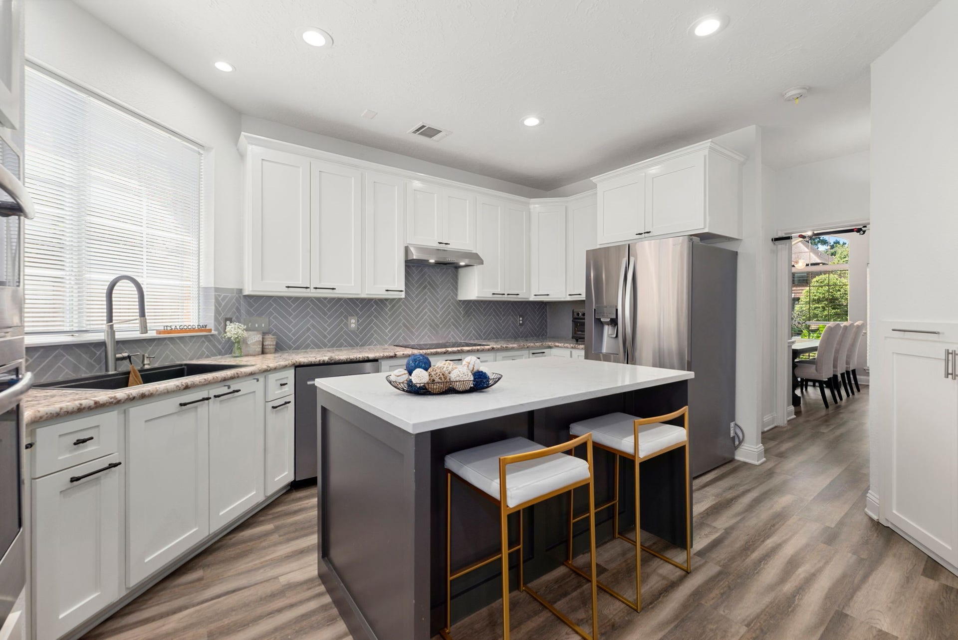 Bright and modern kitchen featuring sleek white cabinetry, a stylish herringbone backsplash, and a spacious island , seamlessly flowing into the dining area.
