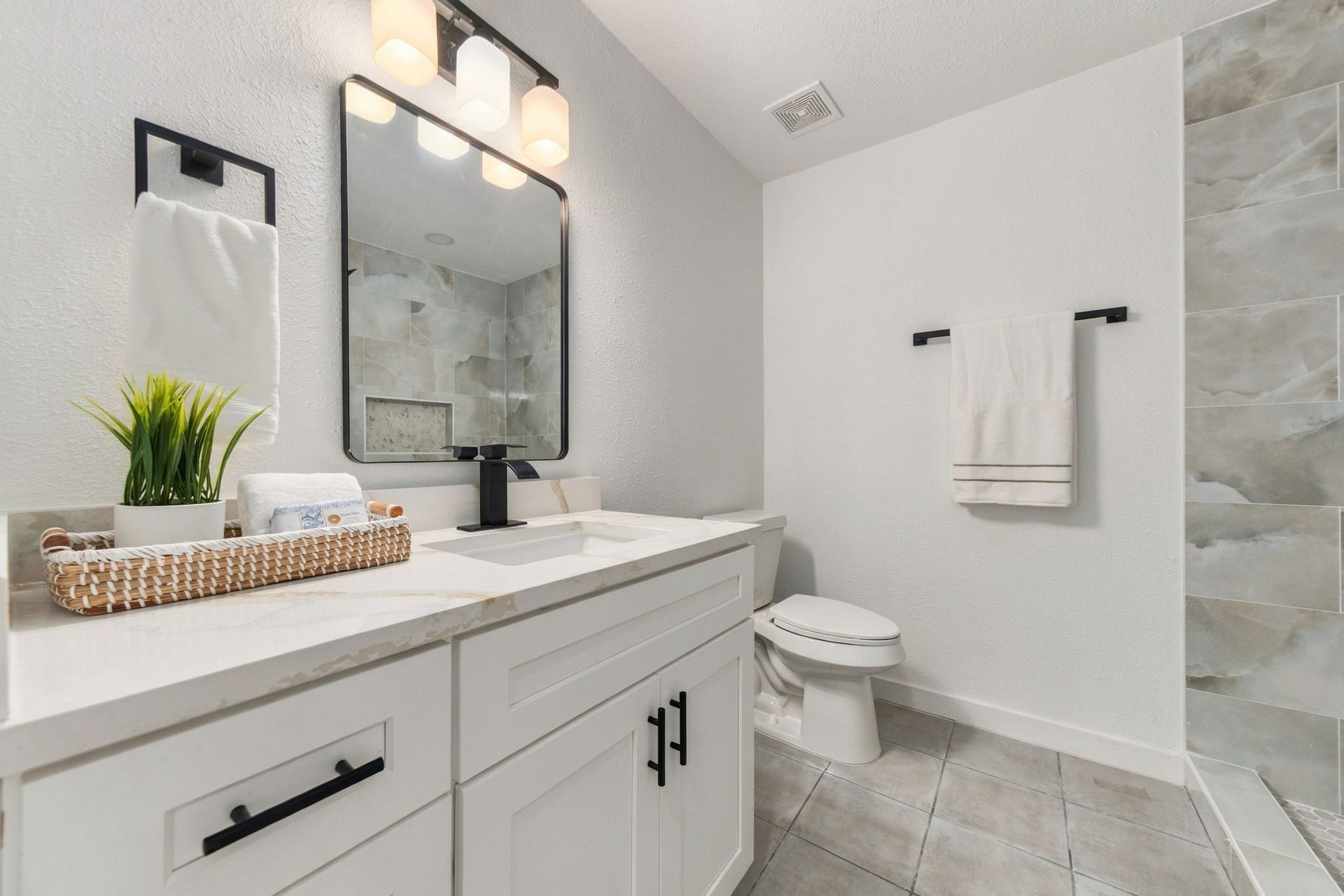 Beautifully renovated bathroom featuring updated cabinetry, fixtures, mirrors, quartz countertops, and lighting.