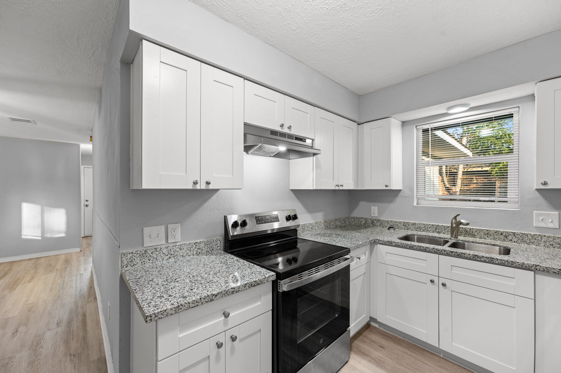 4802 Hannas Reef Drive, Bacliff, TX 77518 This inviting kitchen combines white shaker-style cabinetry, granite countertops, a stainless steel electric range, and a double-basin sink beneath a window overlooking the backyard.