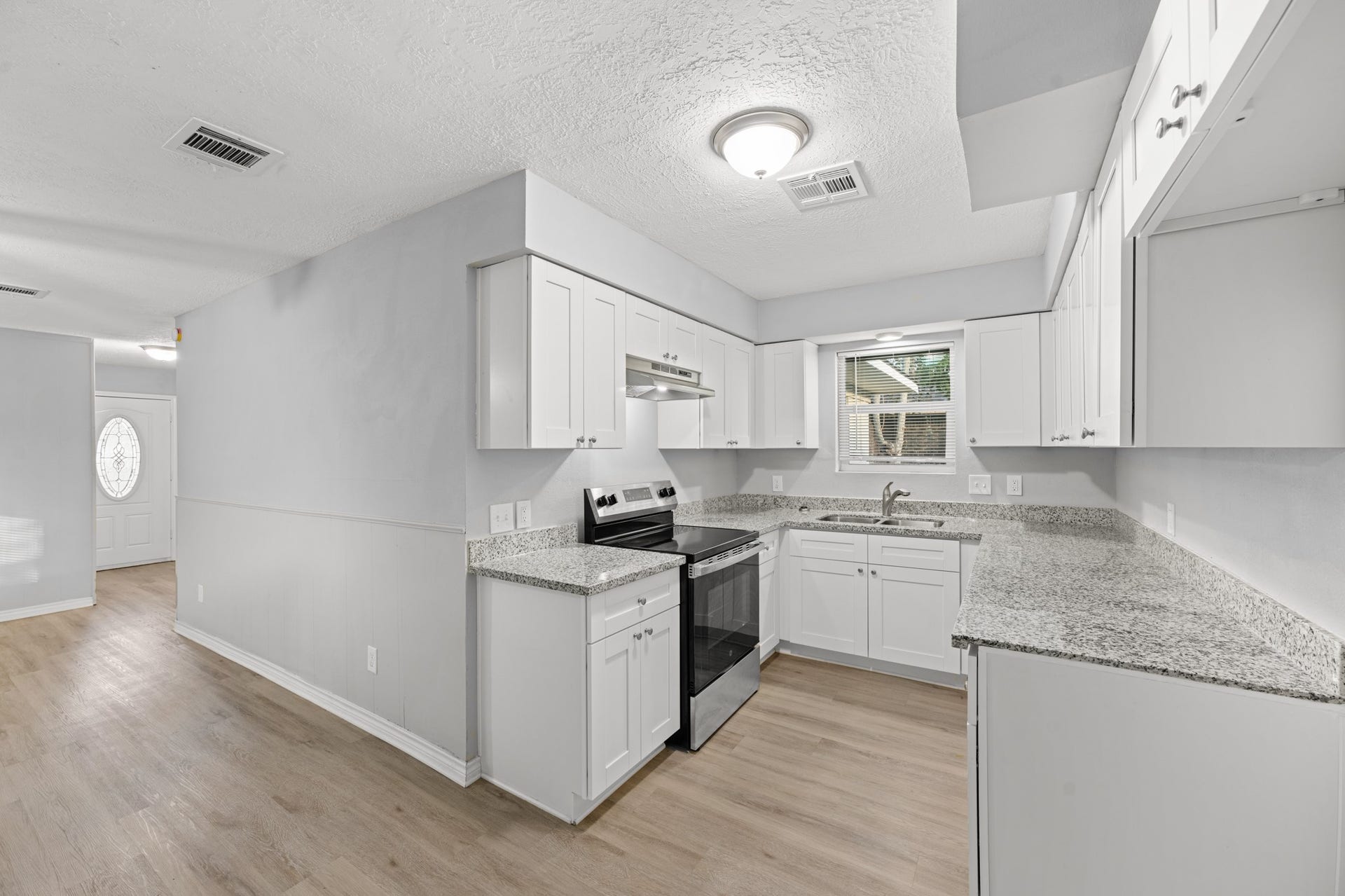 4802 Hannas Reef Drive, Bacliff, TX 77518 The beautifully updated kitchen features white shaker-style cabinetry, granite countertops, stainless steel appliances, and wood-look flooring, with an open connection to the adjoining living area.