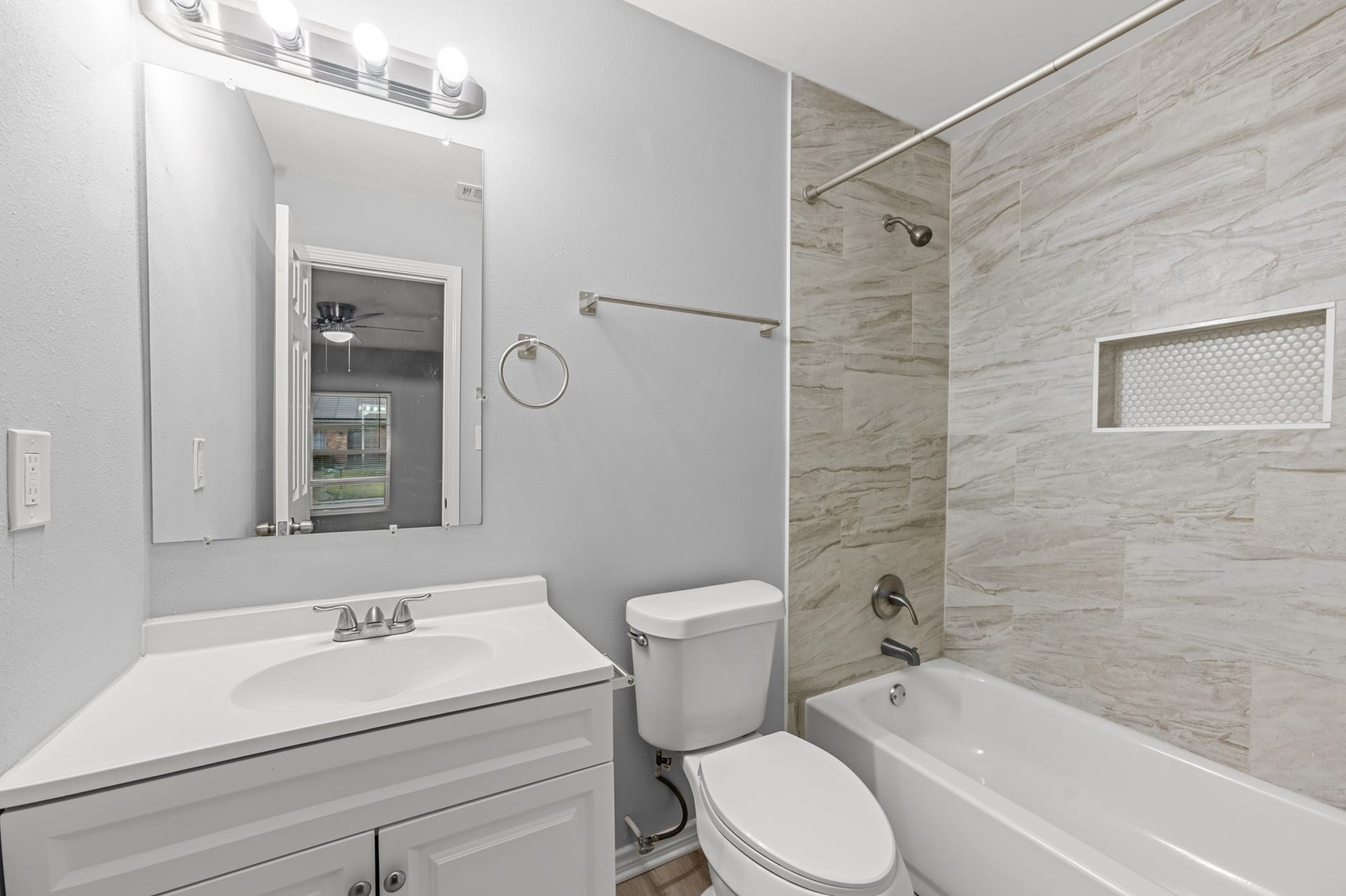 4802 Hannas Reef Drive, Bacliff, TX 77518 The private primary bathroom features a white vanity, tub and shower combination with marble-look tile surround, built-in shower niche, and brushed nickel fixtures for a fresh, modern appearance.