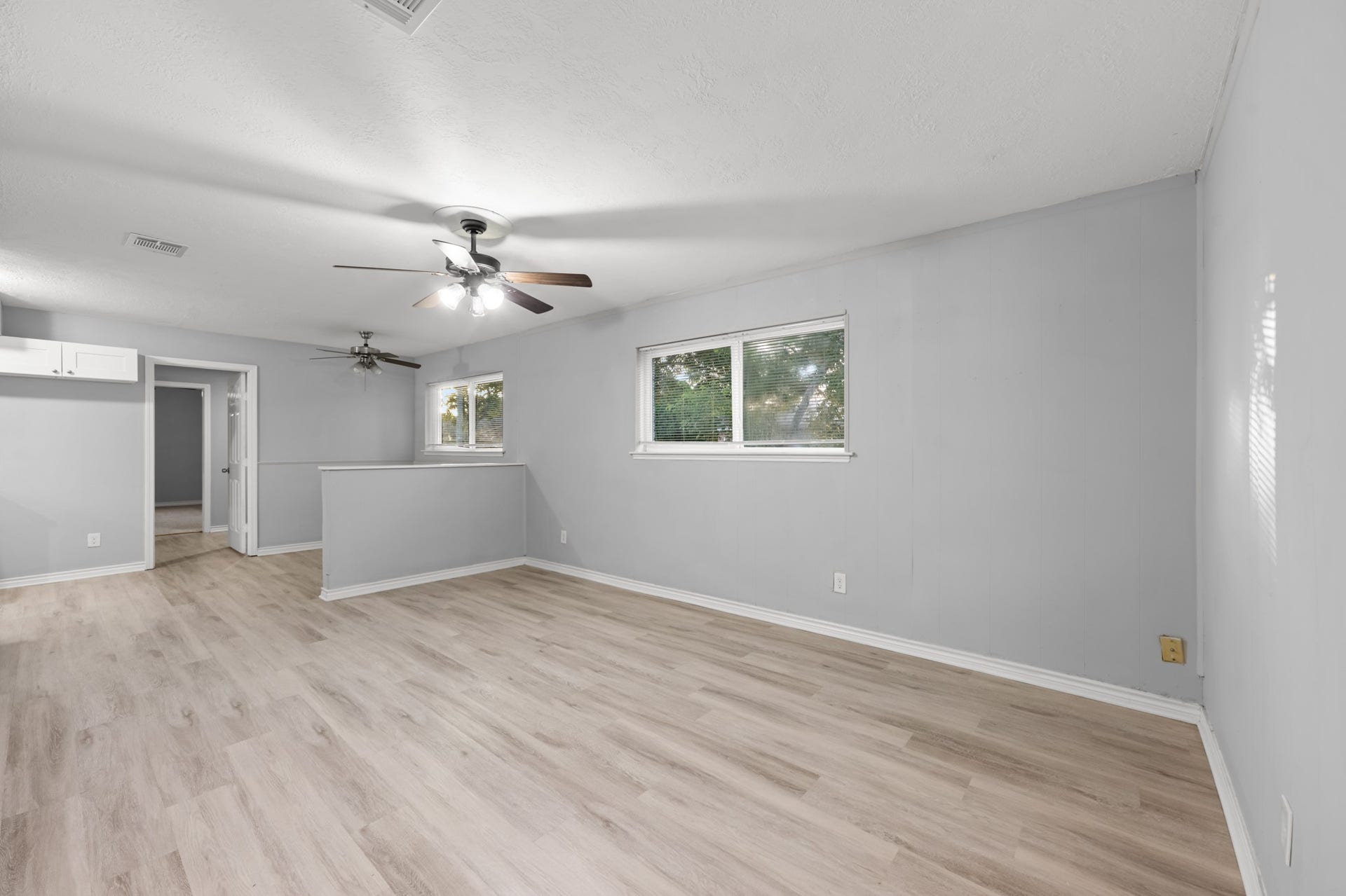 4802 Hannas Reef Drive, Bacliff, TX 77518 The spacious living room offers an inviting setting with wood-look flooring, neutral finishes, ceiling fan, and large windows that fill the space with natural light.