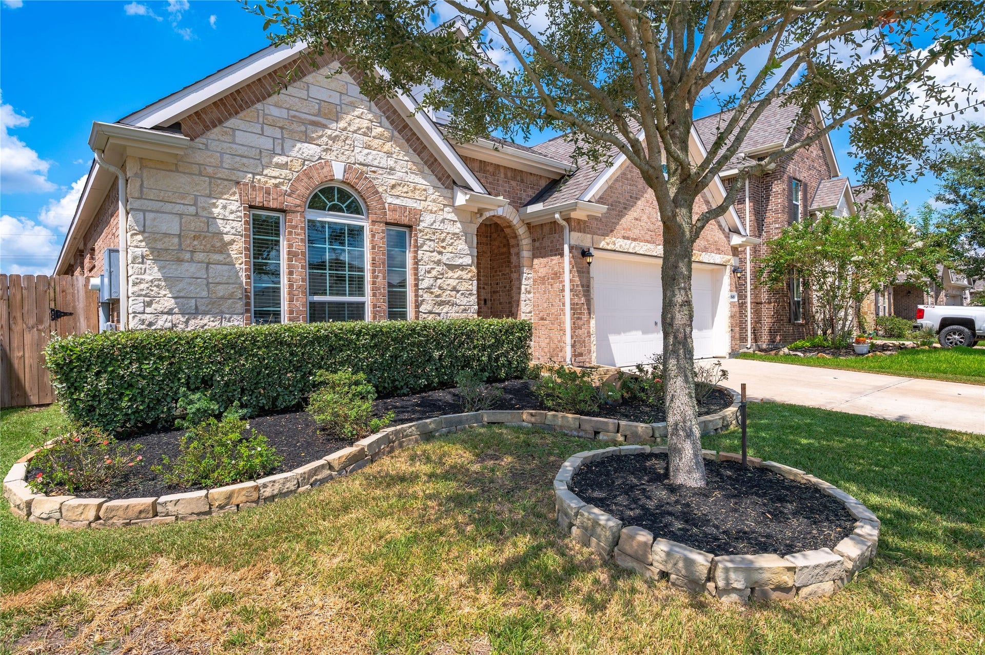 1849 Kenley Way, Alvin, TX 77511 Charming brick and stone home with elegant arched windows, framed by manicured landscaping and a welcoming front yard tree.