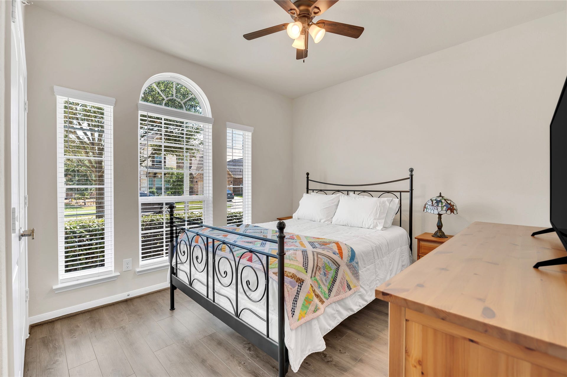 1849 Kenley Way, Alvin, TX 77511 Charming bedroom with a natural light from large arched windows, complemented by a ceiling fan and elegant wood flooring.