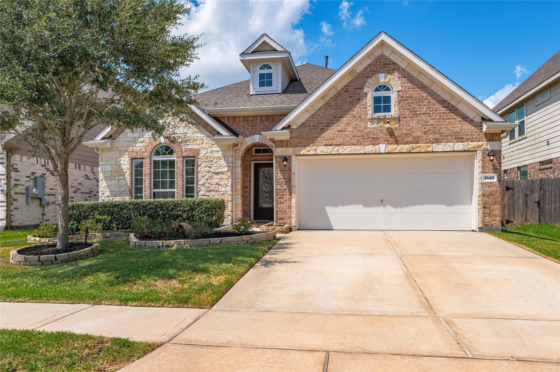 1849 Kenley Way, Alvin, TX 77511 Charming brick and stone facade home with a well-maintained front yard, featuring a spacious driveway and a two-car garage.