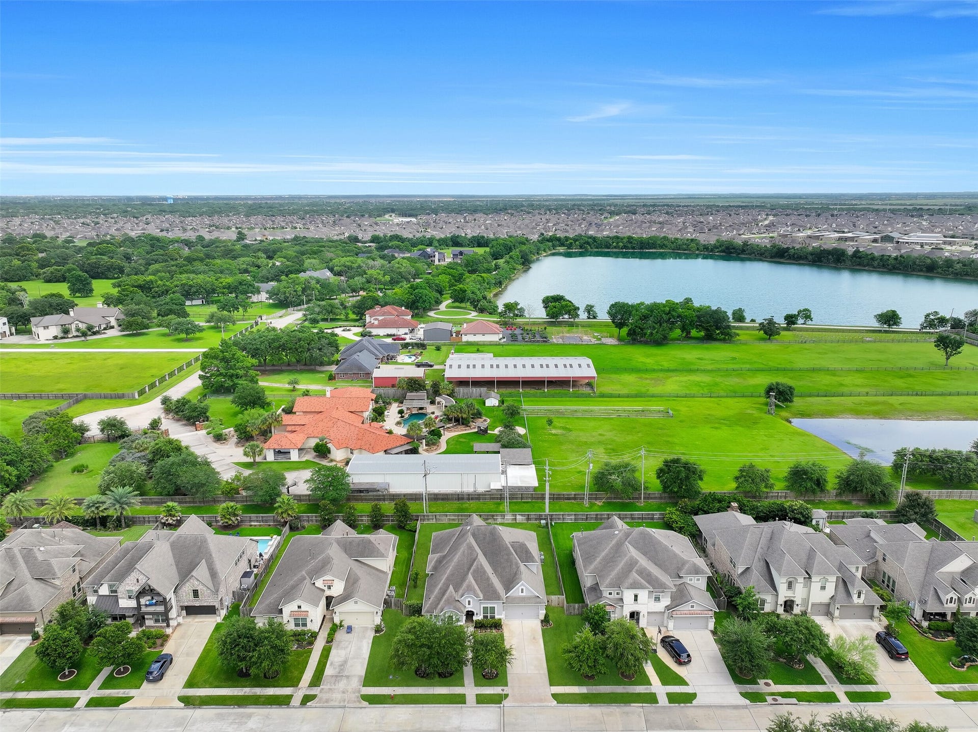 Aerial perspective showcasing the home's position within West Ranch and the unique setting beyond the backyard. Enjoy views toward neighboring Rancho Viejo acreage properties and a glimpse of beautiful spring-fed Lake Friendswood in the distance, creating a rare sense of openness and green space not often found in a master-planned community.