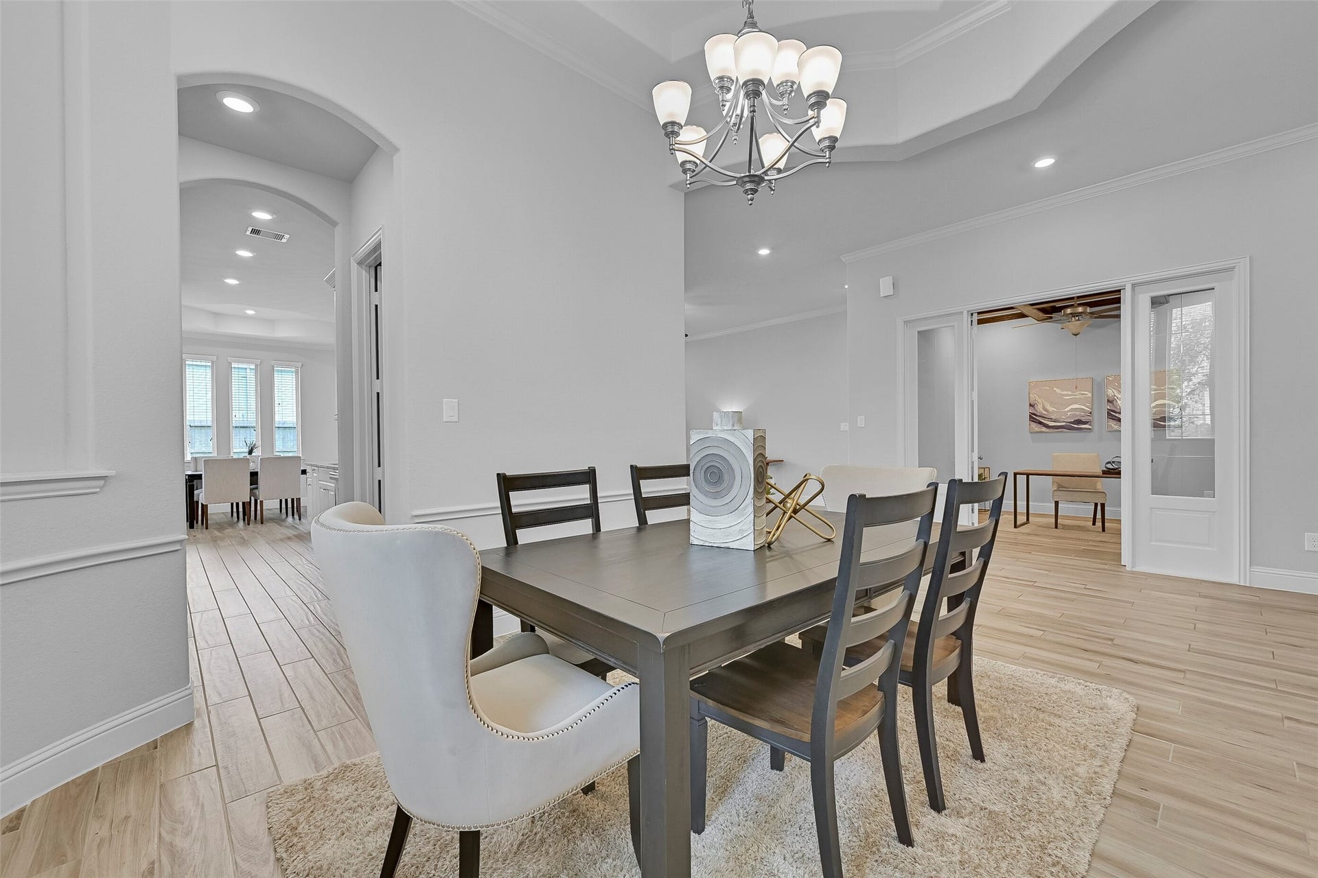 The formal dining room offers an elegant setting for gatherings with its 13-foot tray ceiling, crown and chair molding, oversized windows, wood-look tile flooring, and an updated nine-light chandelier. Convenient access to the butler's pantry provides a seamless connection to the kitchen.