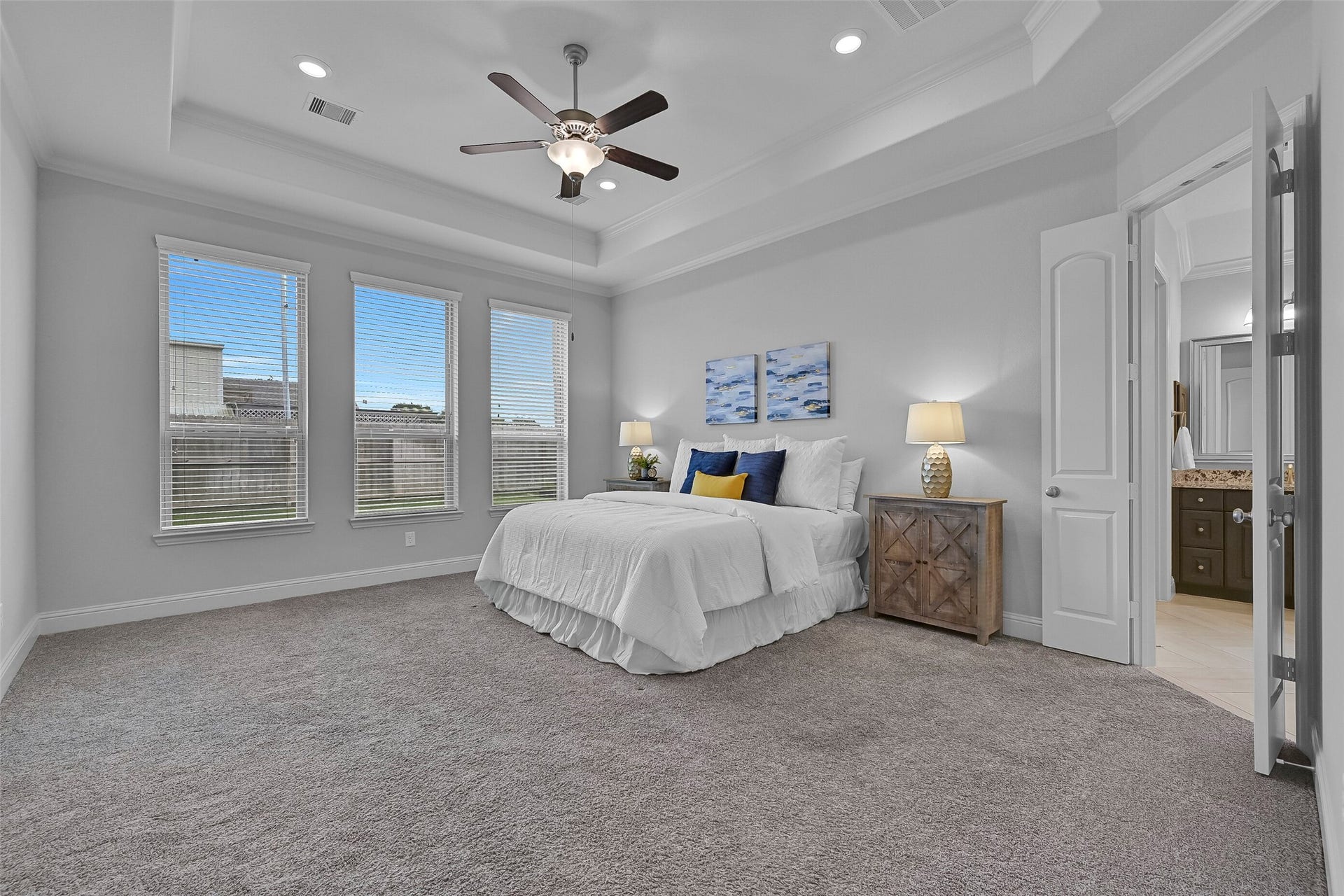 Tucked away at the rear of the home, the spacious primary suite offers an 11-foot tray ceiling trimmed with crown molding, recessed lighting, a lighted ceiling fan, plush carpet, and three large windows that fill the room with natural light while maintaining privacy.