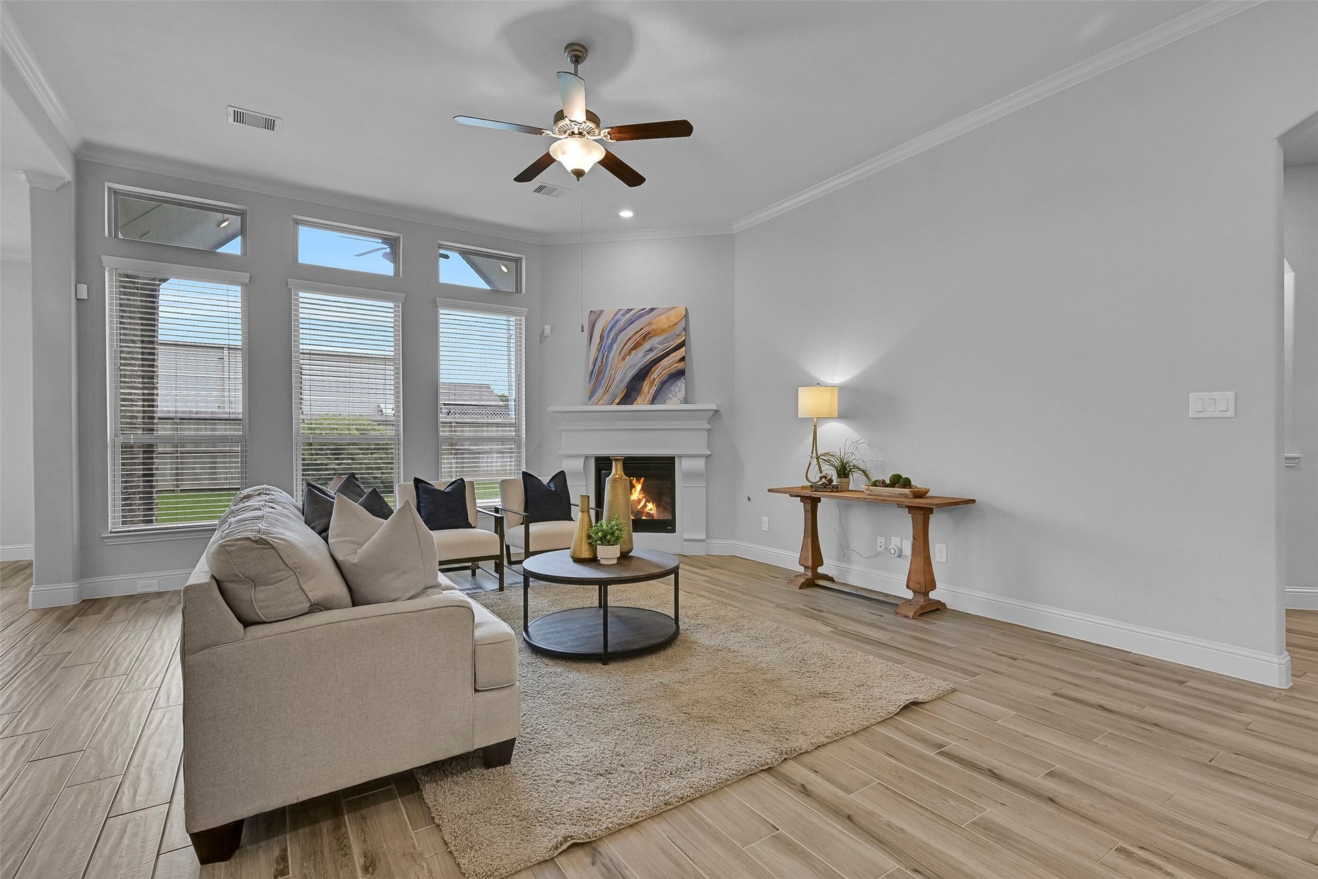 Continue into the spacious family room where soaring ceilings, crown molding, recessed lighting, wood-look tile flooring, and a lighted ceiling fan create an inviting atmosphere. Tall windows and transom windows fill the room with natural light while the cast stone fireplace serves as a beautiful focal point.