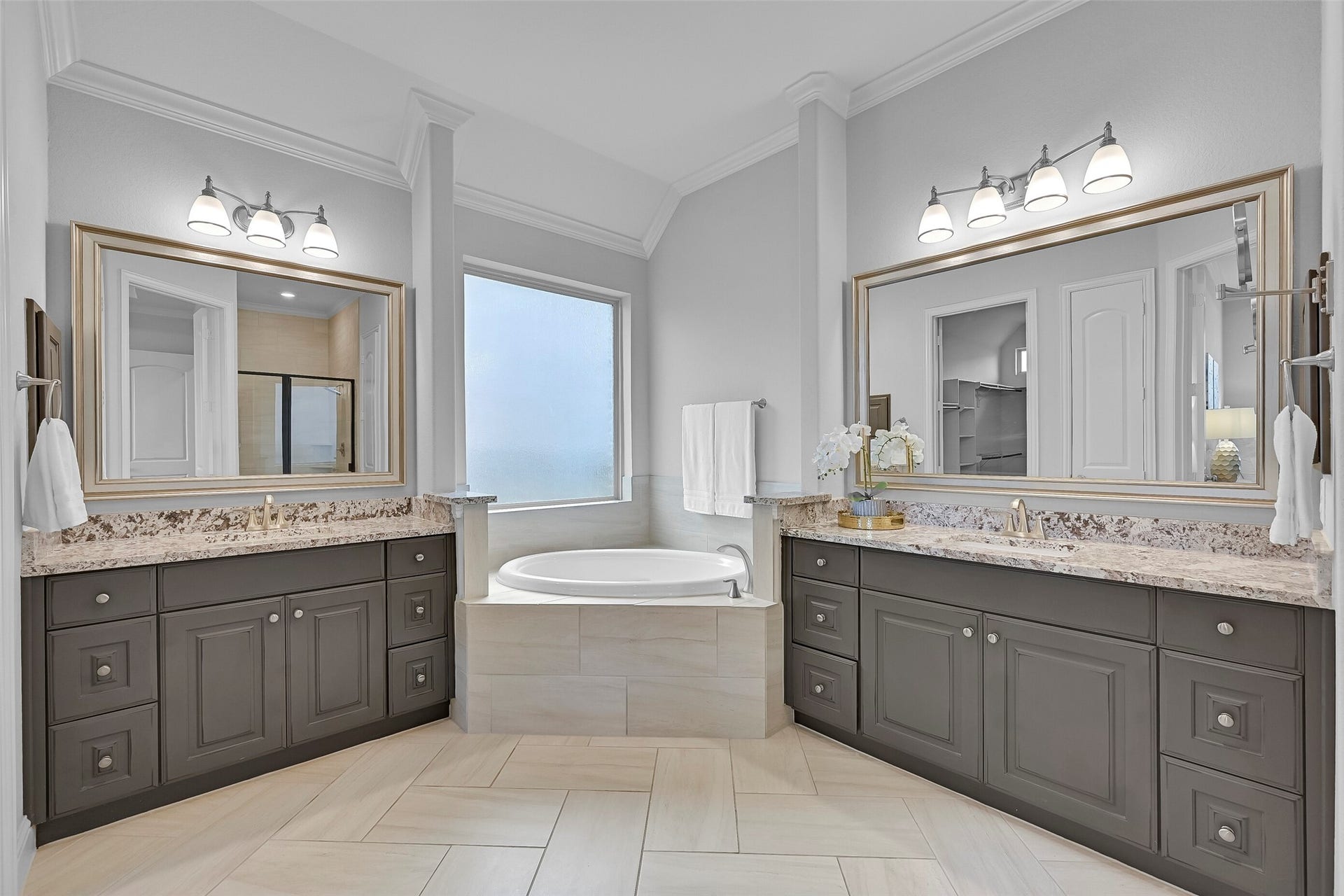 Step into the luxurious ensuite bath showcasing dual granite vanities, framed mirrors, upgraded cabinetry, a relaxing corner soaking tub, and abundant natural light. The thoughtful layout provides plenty of space for busy mornings while maintaining a spa-like feel.