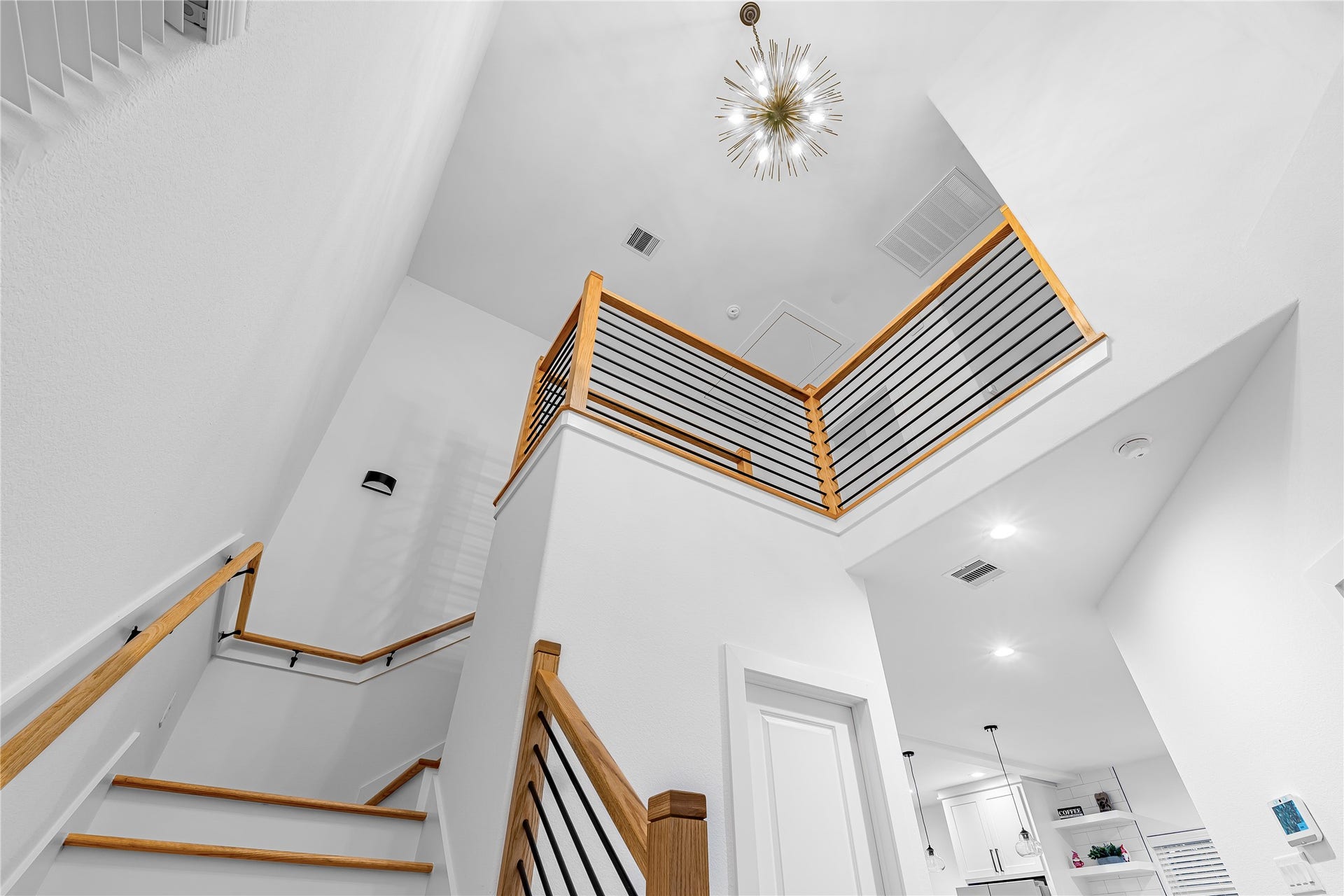7107 Foster Street, #B, Houston, TX 77021 Stunning modern staircase with sleek wood and metal railings, highlighted by an elegant chandelier, leads to an airy upper level.
