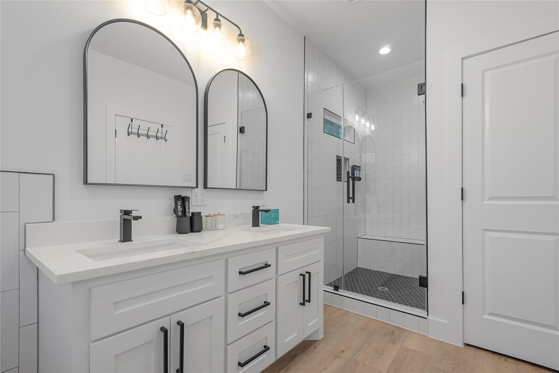 7107 Foster Street, #B, Houston, TX 77021 Sleek and modern bathroom featuring a double vanity with elegant arched mirrors, stylish black fixtures, and a spacious glass-enclosed shower with a built-in bench.