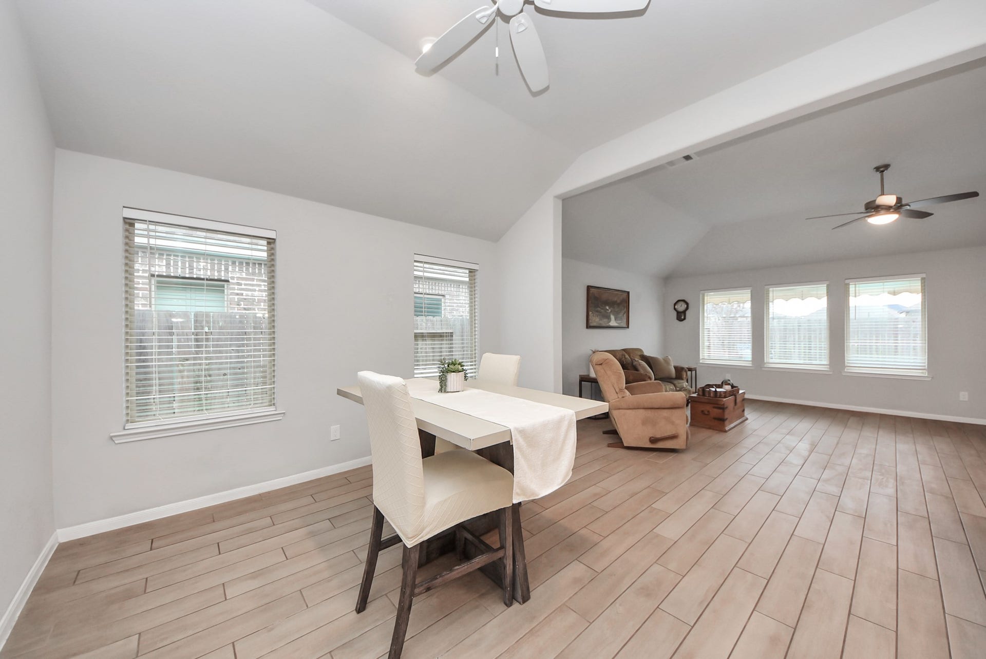 Bright open-concept living space featuring a dining area and a cozy seating area. The room is enhanced by large windows, light wood flooring, and ceiling fans, creating a welcoming and airy atmosphere.