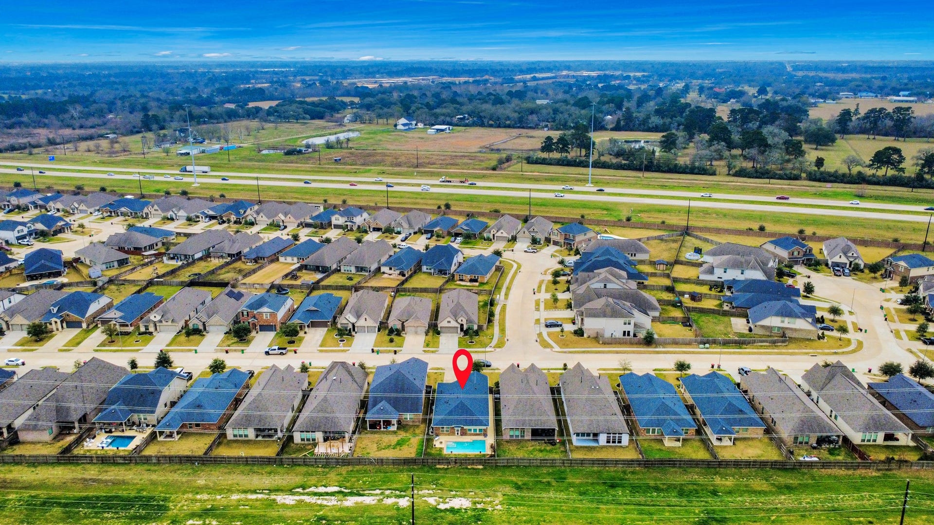This aerial photo showcases a suburban neighborhood with neatly arranged homes, each with spacious backyards. A highlighted house features a swimming pool, indicating a desirable amenity. The community is bordered by a major road, offering easy access to surrounding areas.