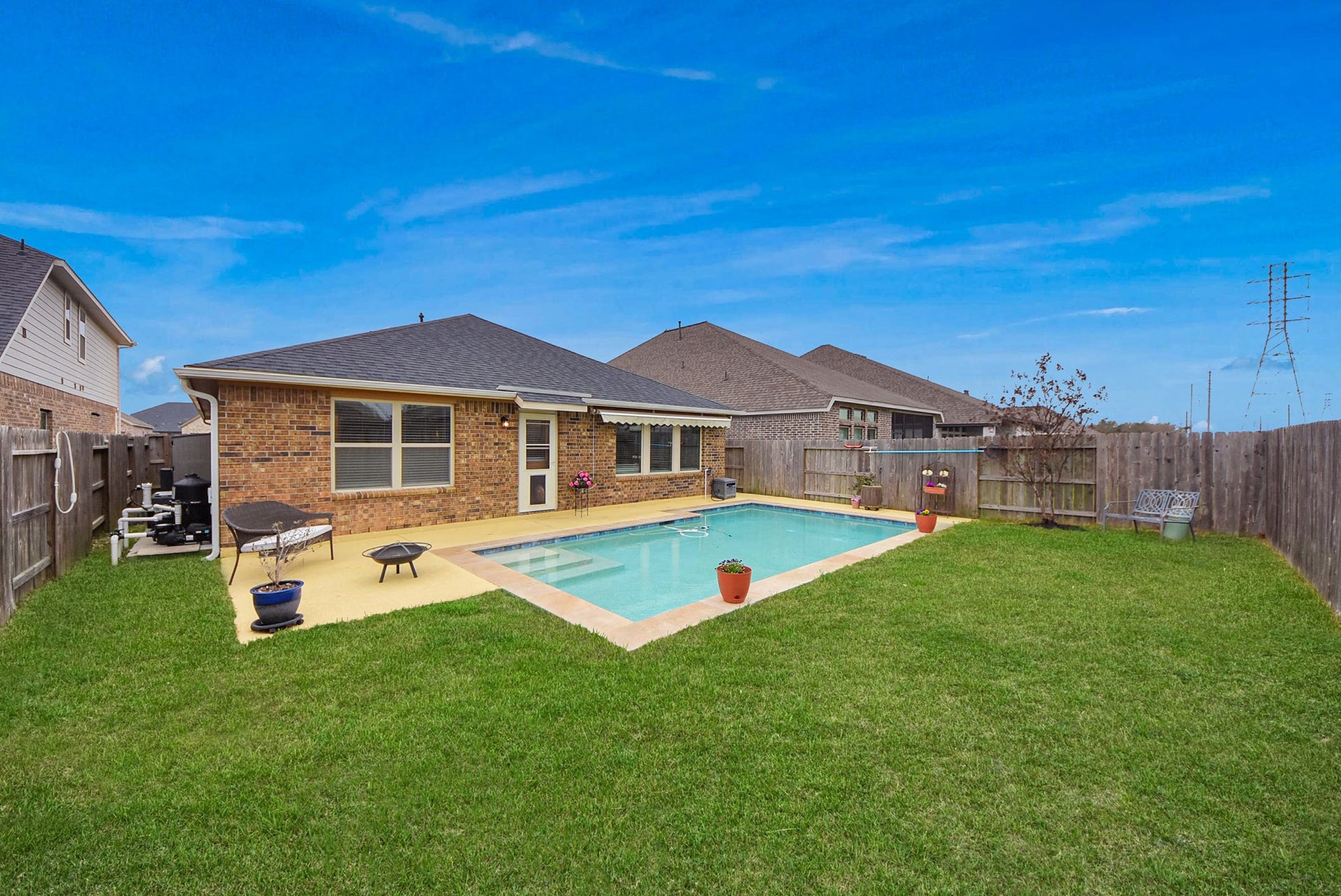 This photo showcases a charming single-story brick home with a well-maintained backyard featuring a swimming pool. The pool is surrounded by a concrete patio and lush green lawn, enclosed by a wooden fence for privacy. The area is perfect for outdoor relaxation and entertaining.