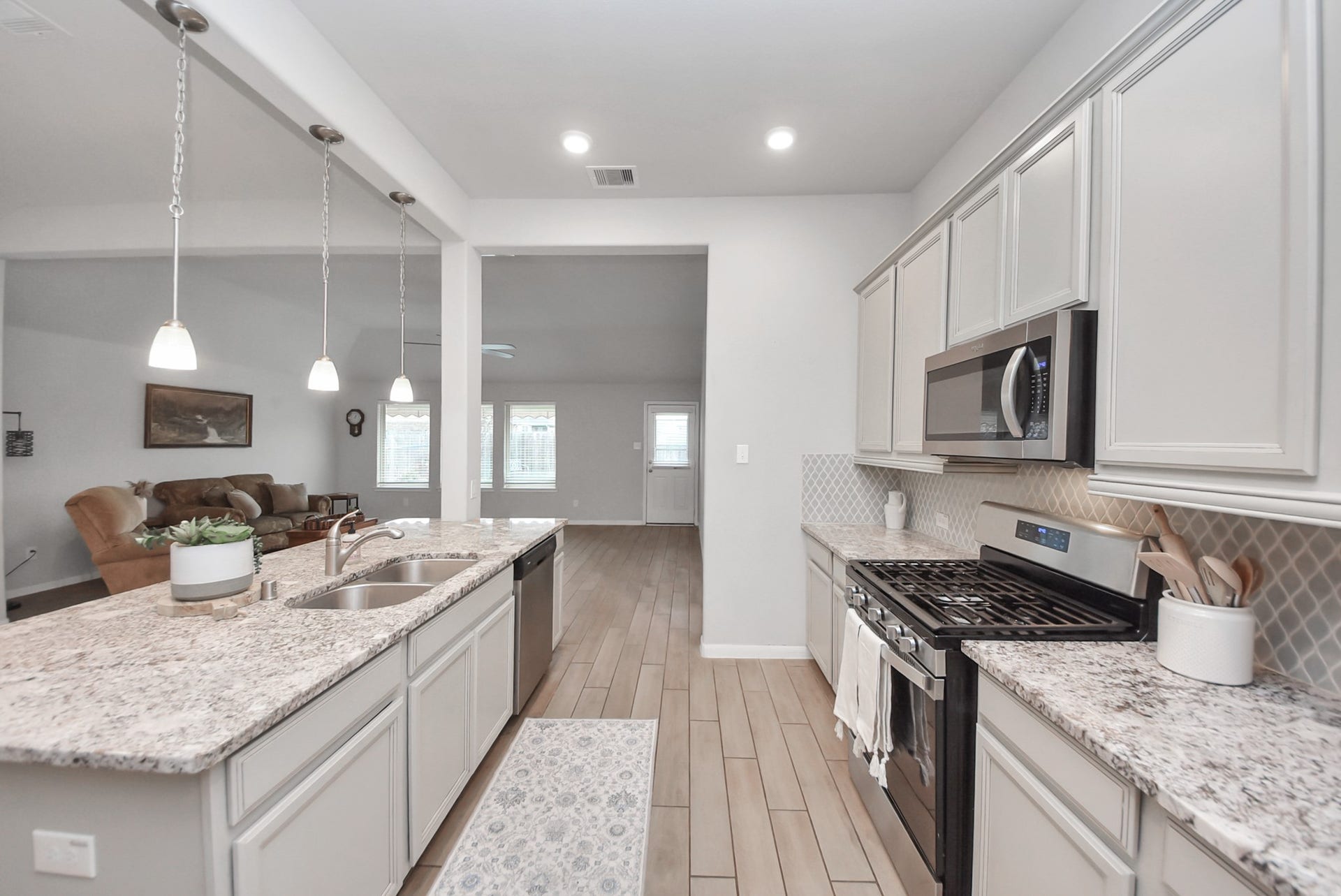 This photo showcases a modern kitchen with granite countertops, stainless steel appliances, and ample cabinetry. The open-concept design flows into a spacious living area, highlighted by pendant lighting and large windows for natural light.