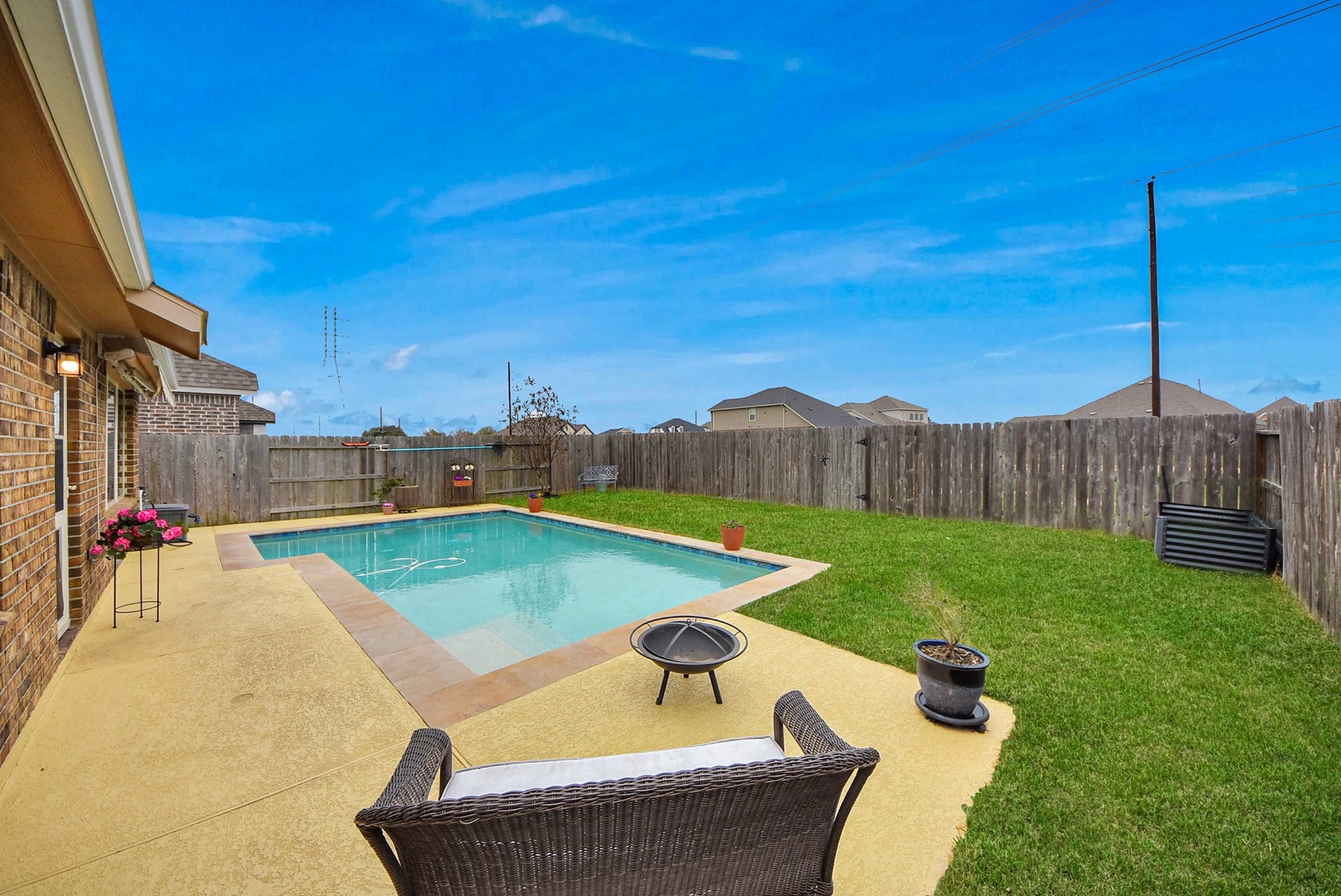 This backyard features a cozy swimming pool surrounded by a privacy fence, with a small grassy area and patio seating, perfect for relaxation and outdoor gatherings.