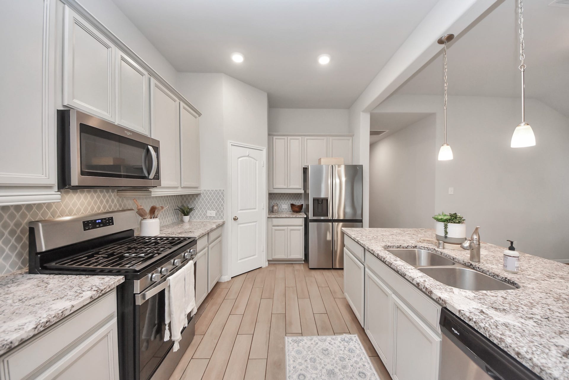This modern kitchen features stainless steel appliances, granite countertops, and ample cabinet space. It has a gas stove, built-in microwave, and a double sink. The open layout and pendant lighting add a welcoming touch.