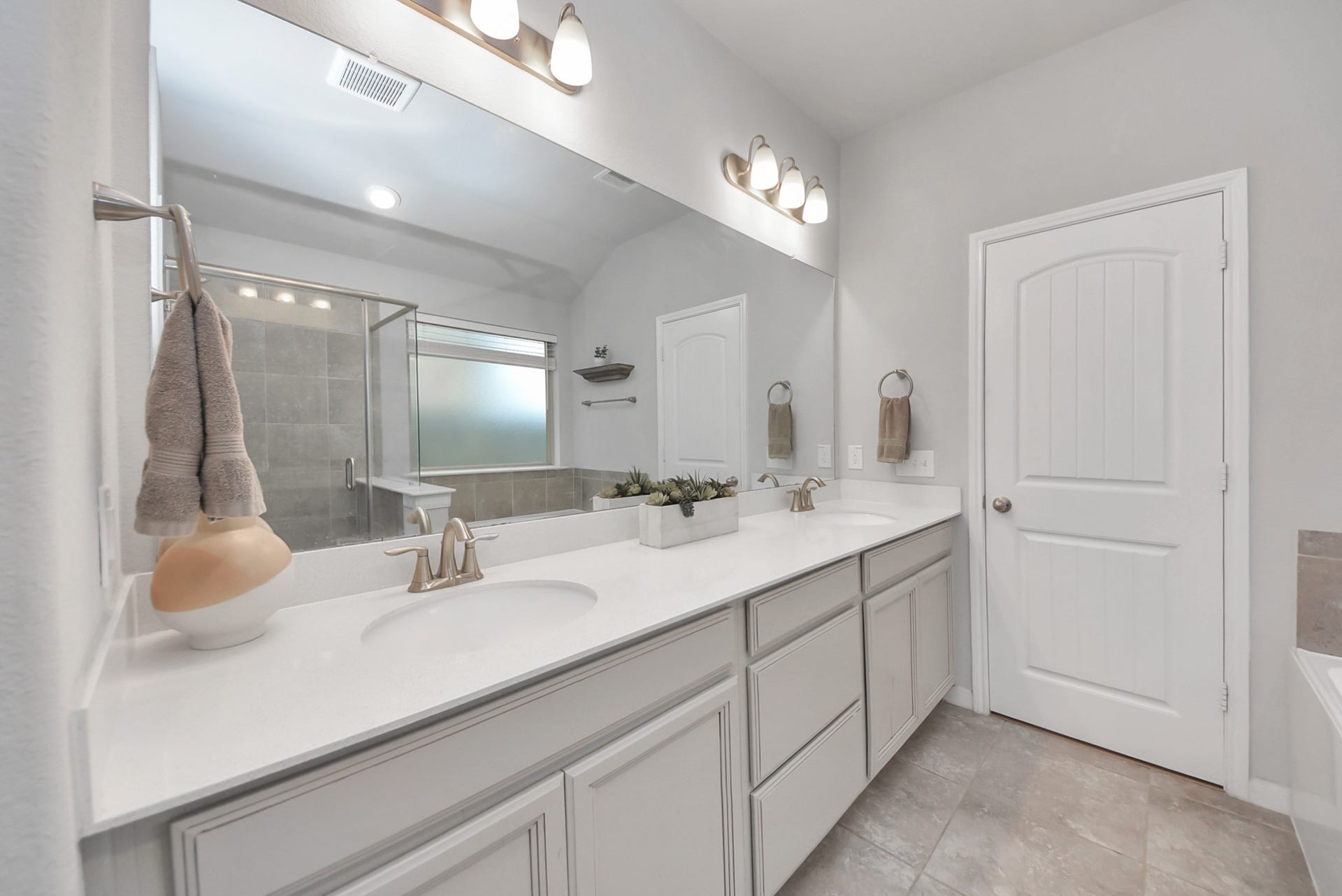 This private bathroom features a modern design with dual sinks, a large mirror, and stylish lighting. It has a glass-enclosed shower, neutral tile flooring, and ample cabinet space for storage. The overall look is sleek and inviting.