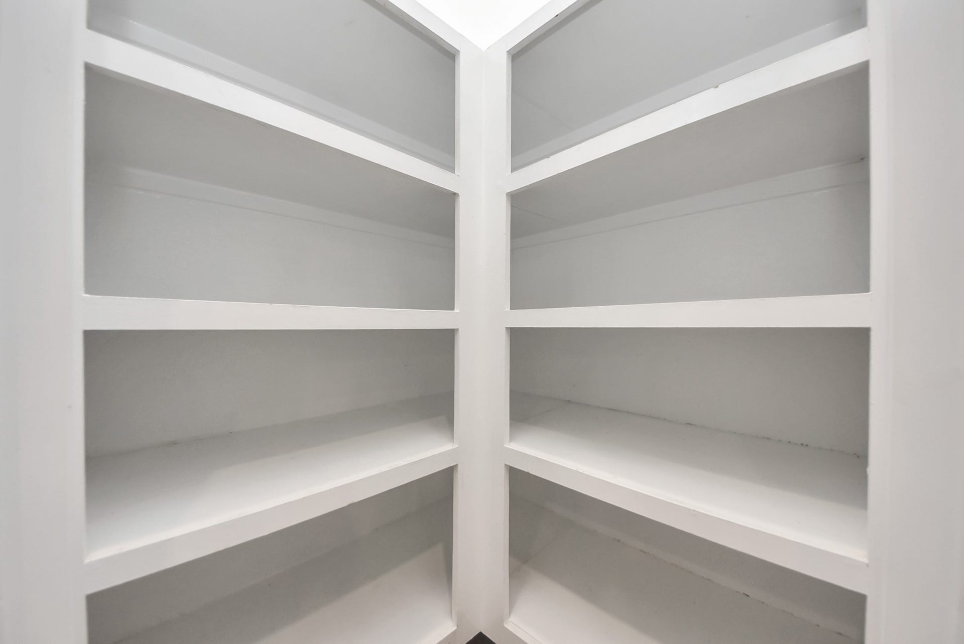 This photo shows a corner pantry with multiple white shelves, offering ample storage space for kitchen essentials.