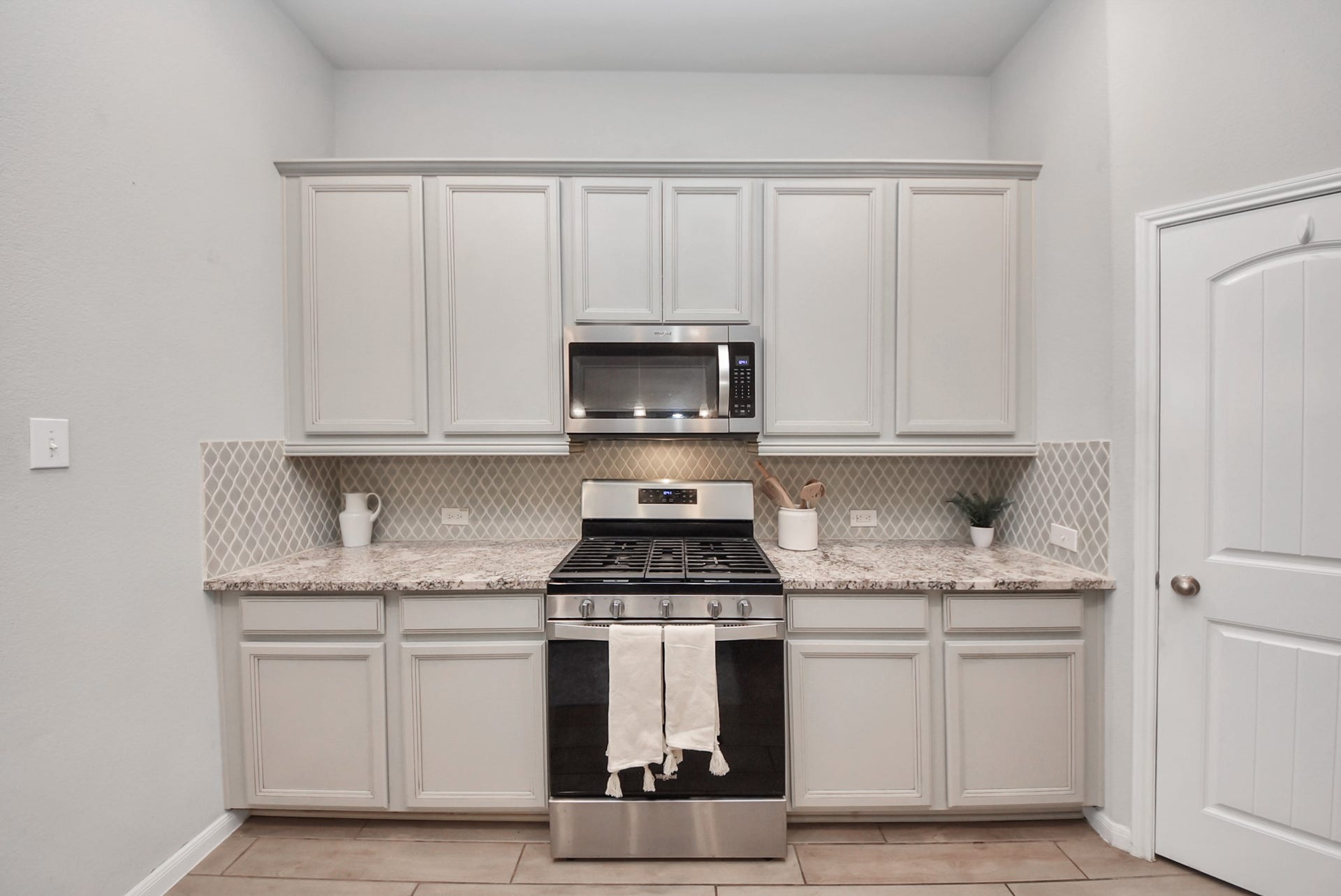 This kitchen features sleek light gray cabinetry, a granite countertop, and a stainless steel gas range with a microwave above. The backsplash has a stylish geometric pattern, and there is ample storage space.