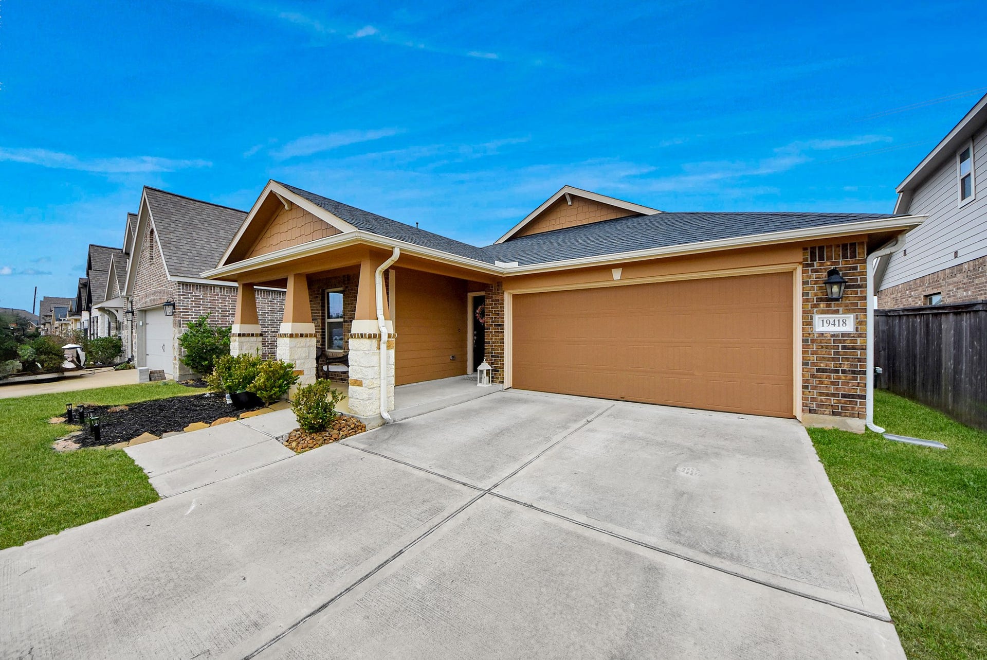 This is a charming single-story home with a brick exterior and a two-car garage. It features a well-maintained front yard with a small garden area and a covered entryway. The driveway is spacious, and the neighborhood appears quiet and inviting.