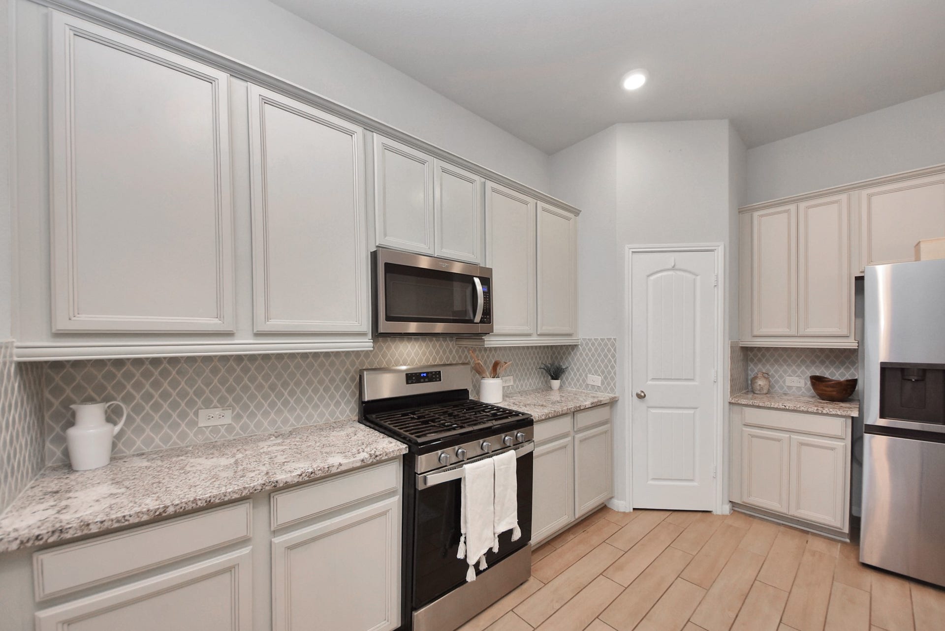 This kitchen features modern stainless steel appliances, ample white cabinetry, and granite countertops. The light color palette and tiled backsplash create a bright, inviting space with plenty of storage.