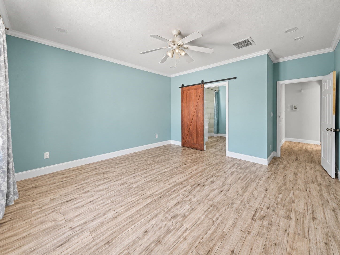 Spacious primary suite with barn style door, crown molding, ceiling fan, and convenient access to the en-suite bath.