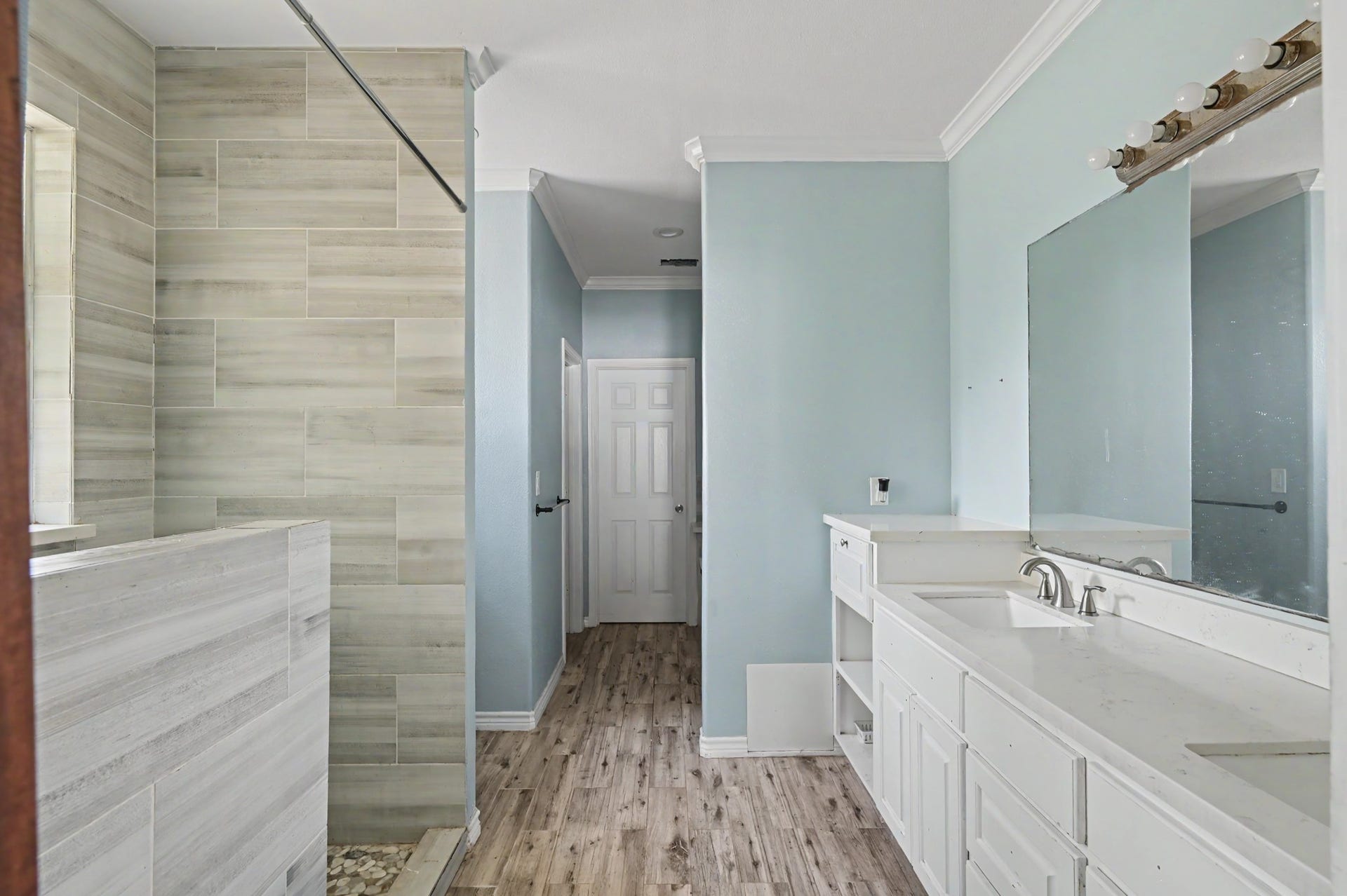 Primary bathroom featuring a large walk-in tiled shower, dual-sink vanity and oversized mirror.