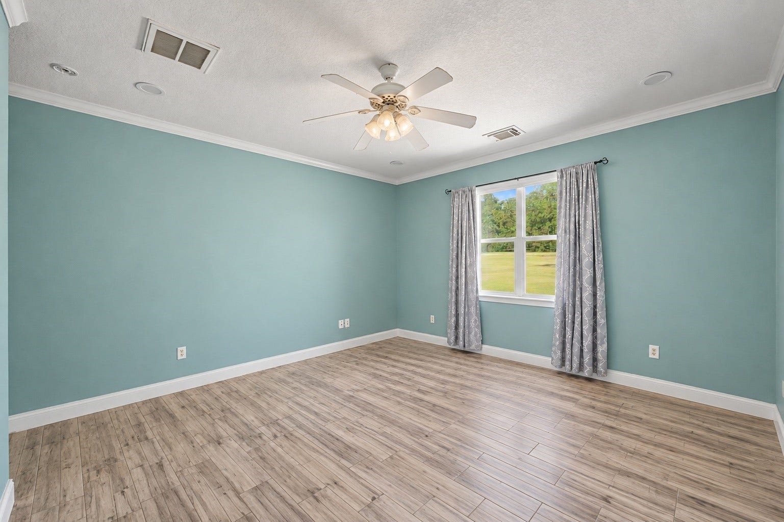 Another view of the spacious primary bedroom with large windows and attractive wood-look tile flooring.