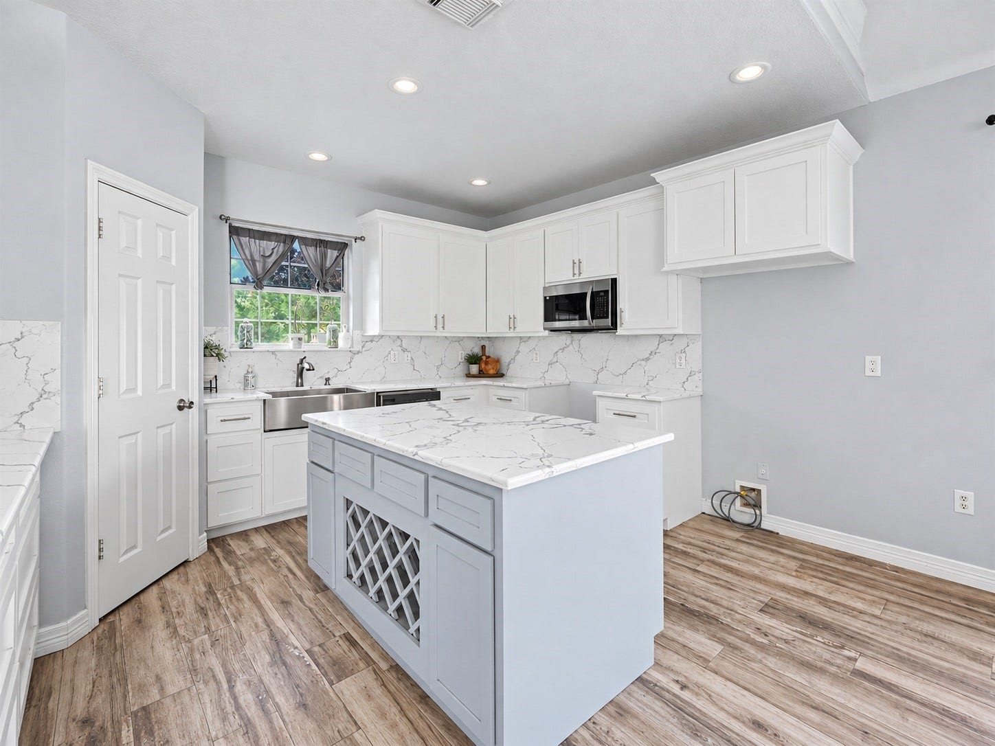 Bright, updated kitchen featuring white cabinetry, stone-loo countertops, recessed lighting, and a center island with built-in wine storage. ***Digitally enhanced kitchen pictures - backsplash needs to be completed