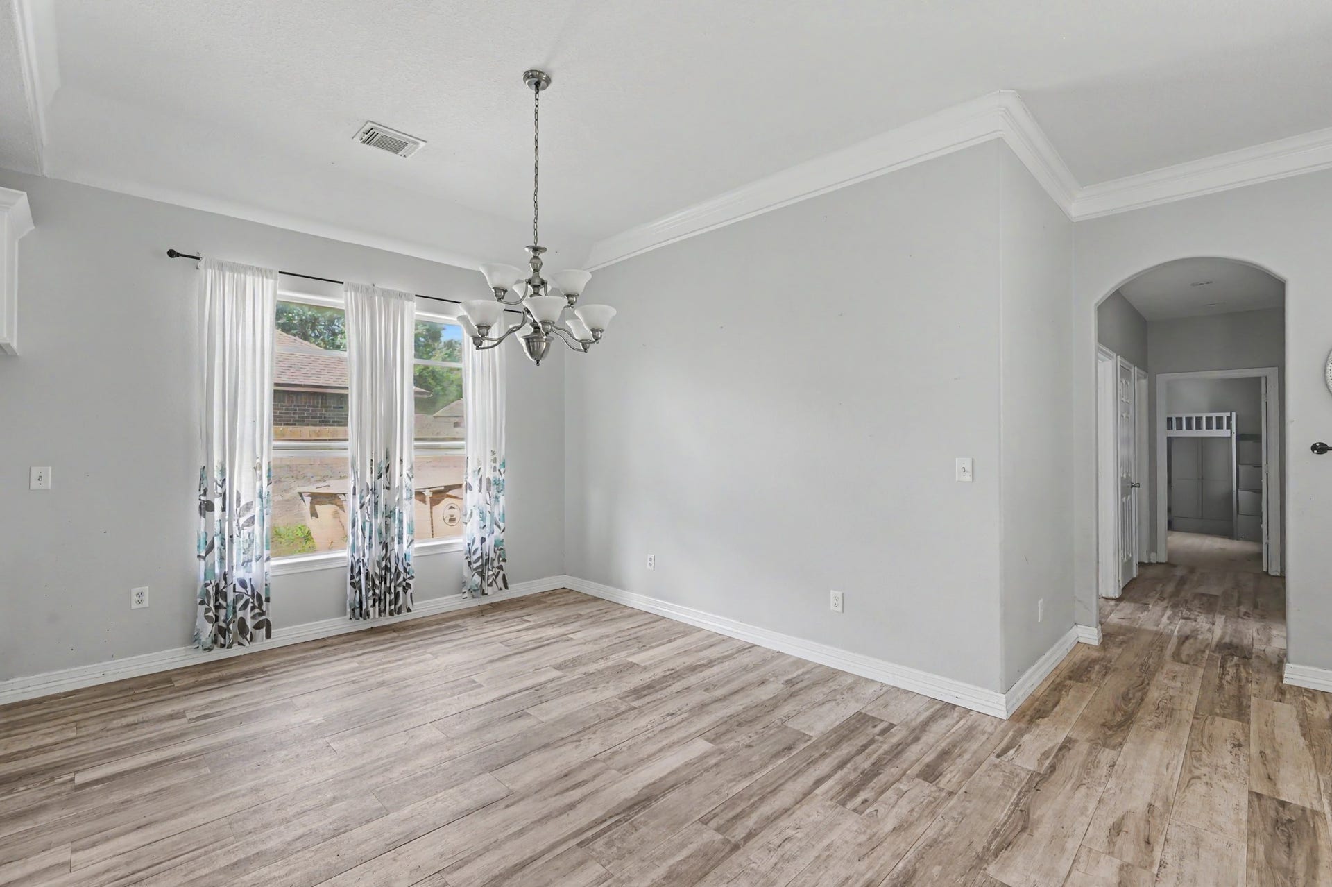 Light-filled dining area with elegant chandelier, crown molding, and direct access to the adjoining hallway and living spaces.
