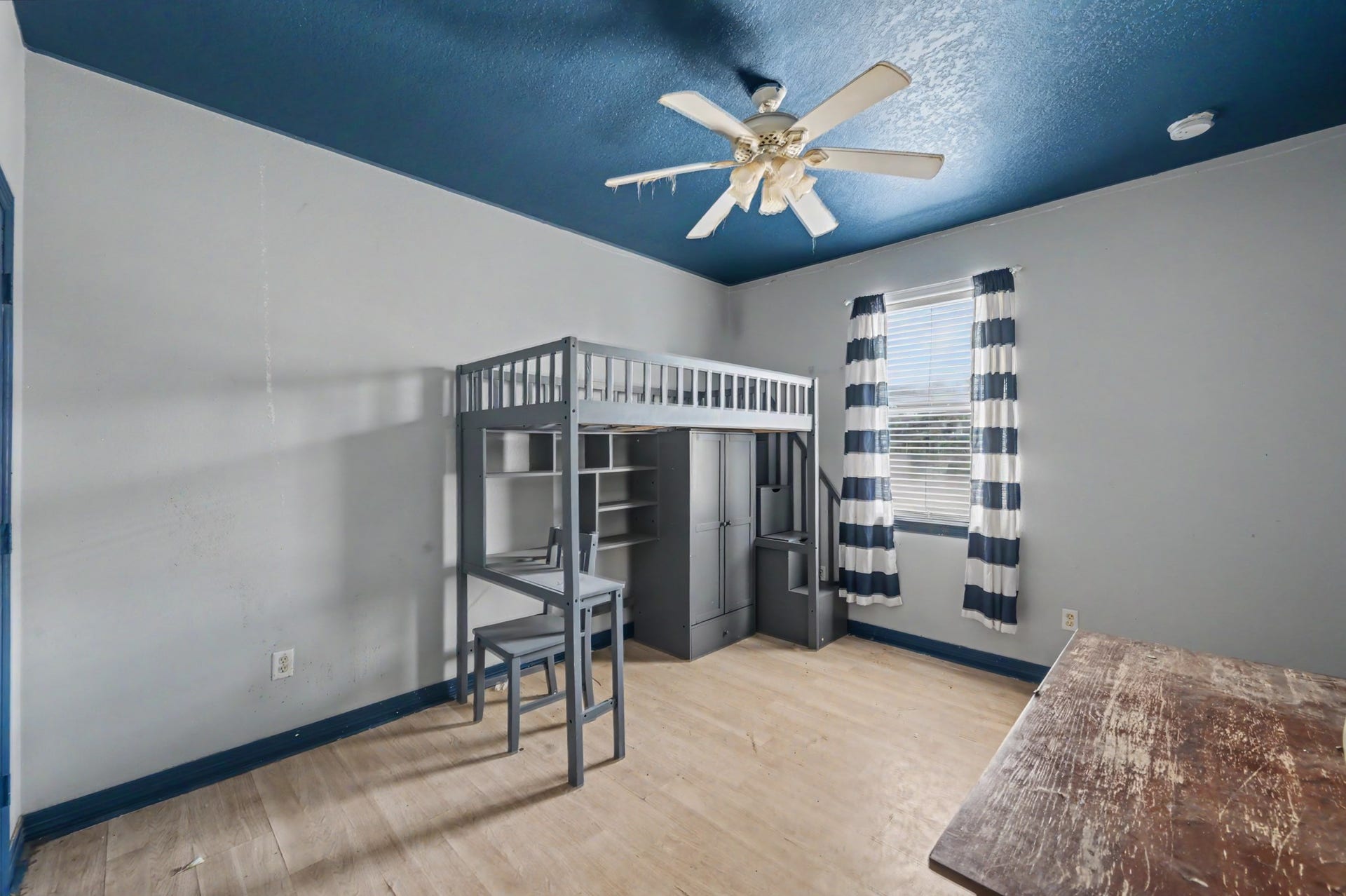 Spacious secondary bedroom featuring a dramatic blue ceiling, ceiling fan, window for natural light, and plenty of room for flexible furniture placement.
