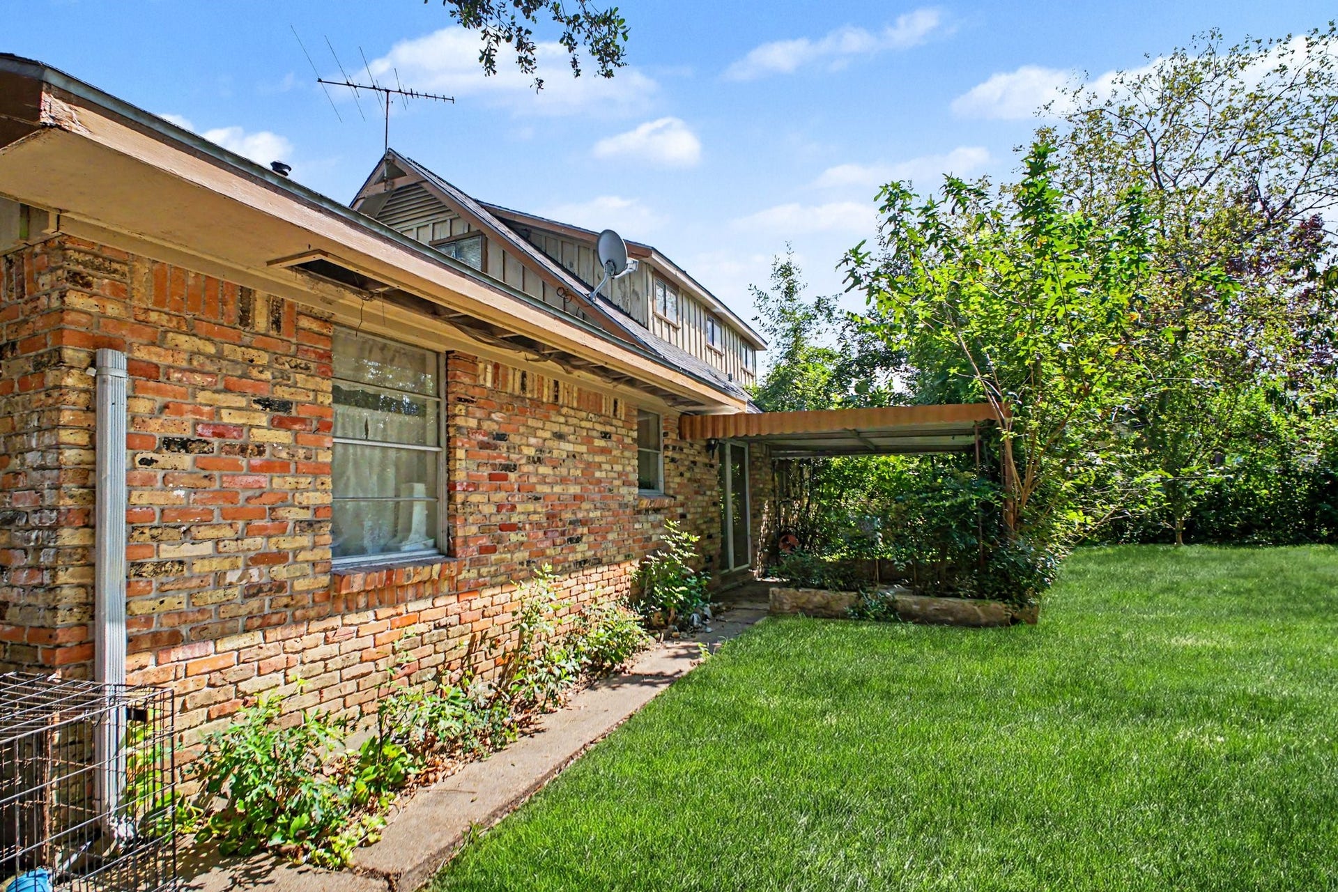 View of the side brick exterior and the well-maintained lawn under bright daylight.
