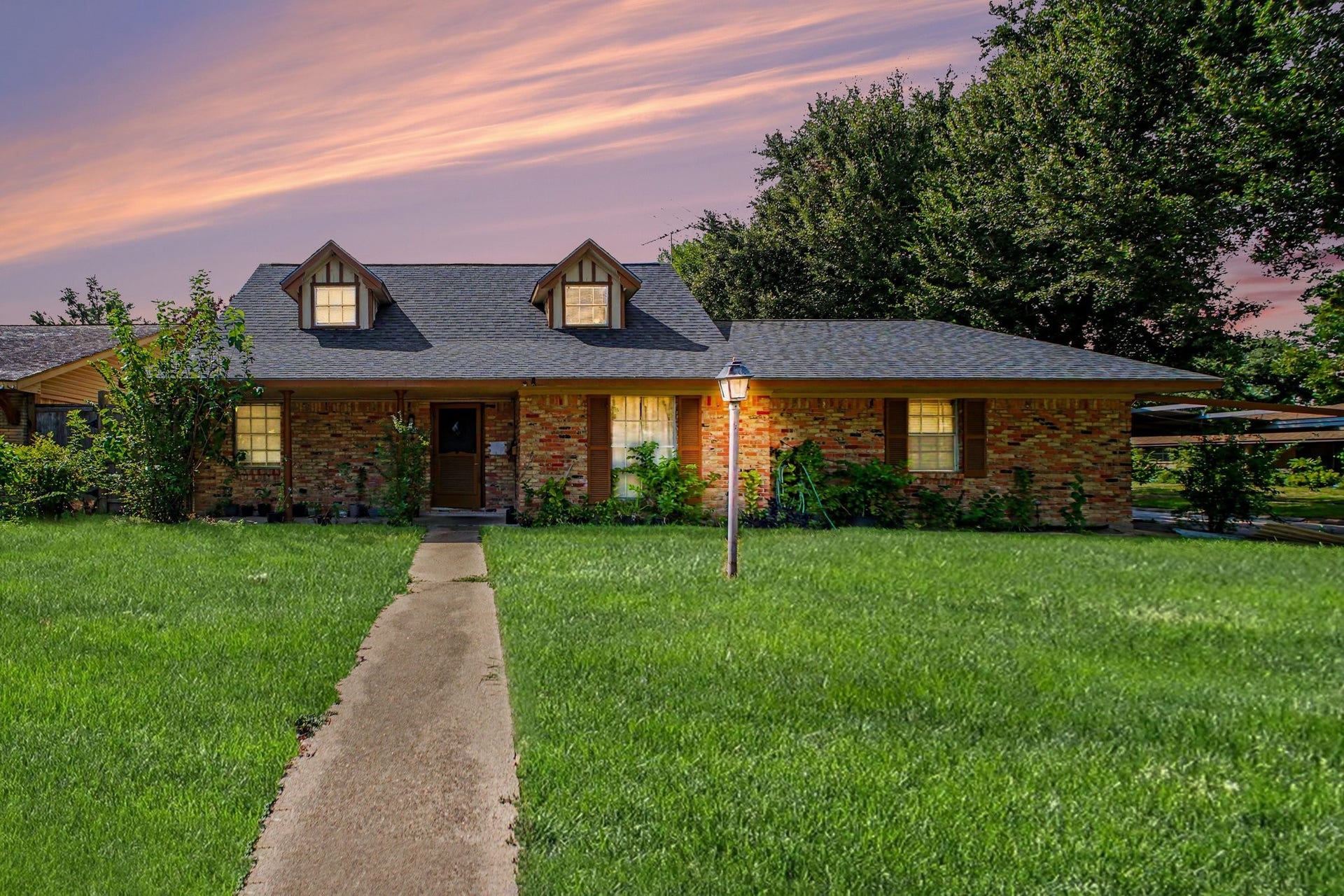 Stunning front exterior view of the brick home featuring a wide manicured lawn under a warm sunset sky.