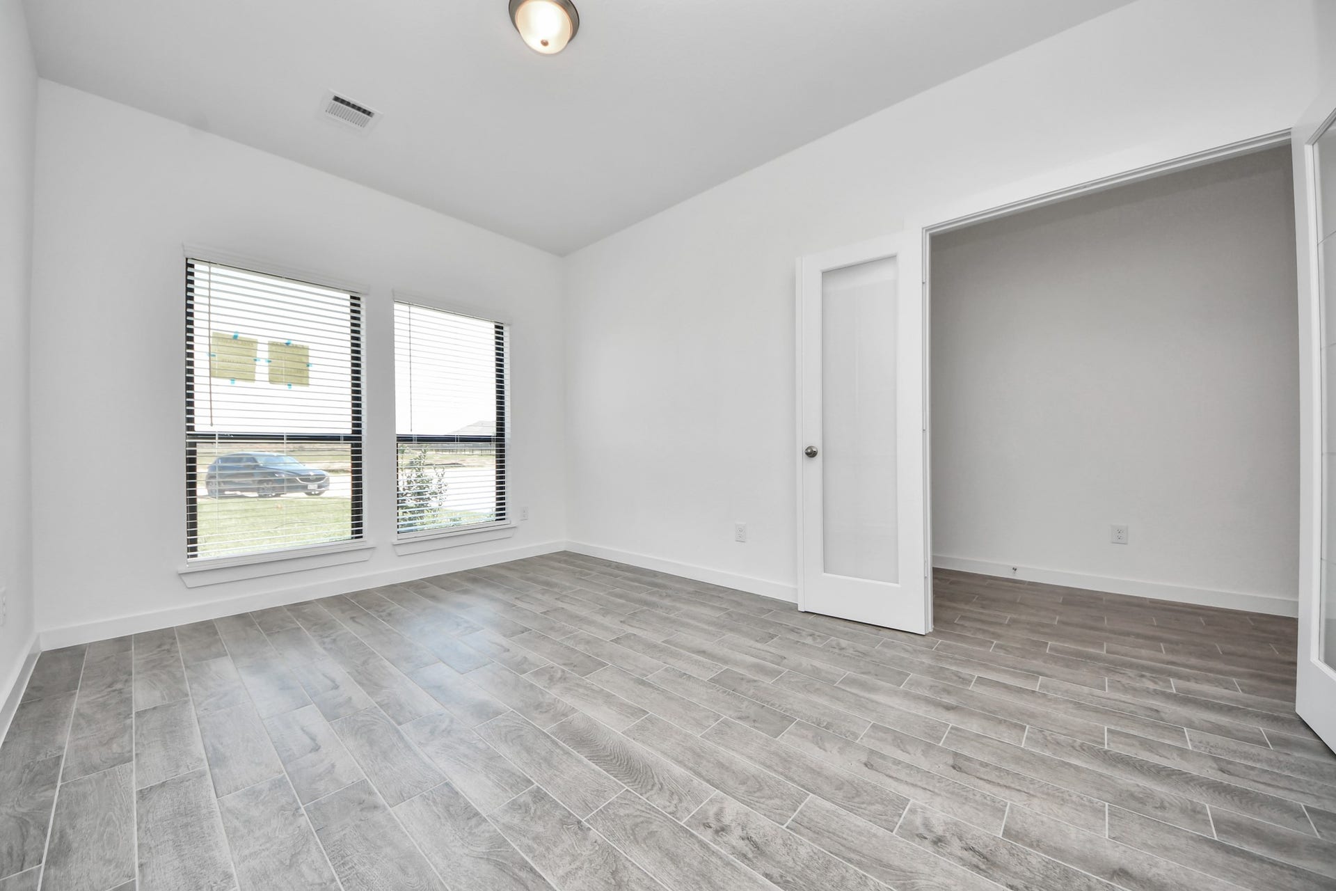 Experience the perfect blend of sophistication and warmth in this home office, boasting elegant wood-look tile flooring and flooded with natural light from expansive windows and French doors.