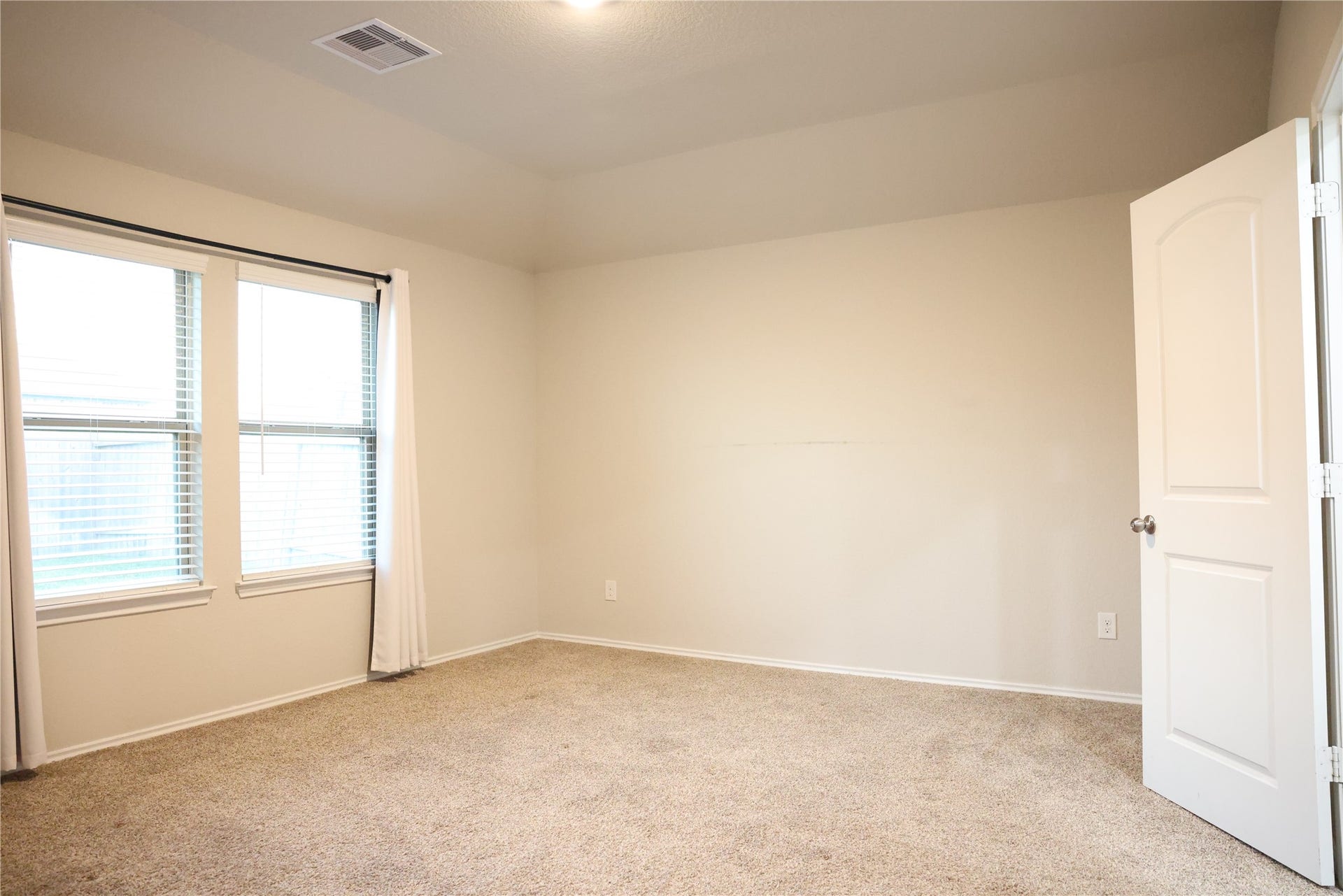 Primary bedroom Bright and inviting bedroom with soft carpeting, neutral walls, and large windows for ample natural light.