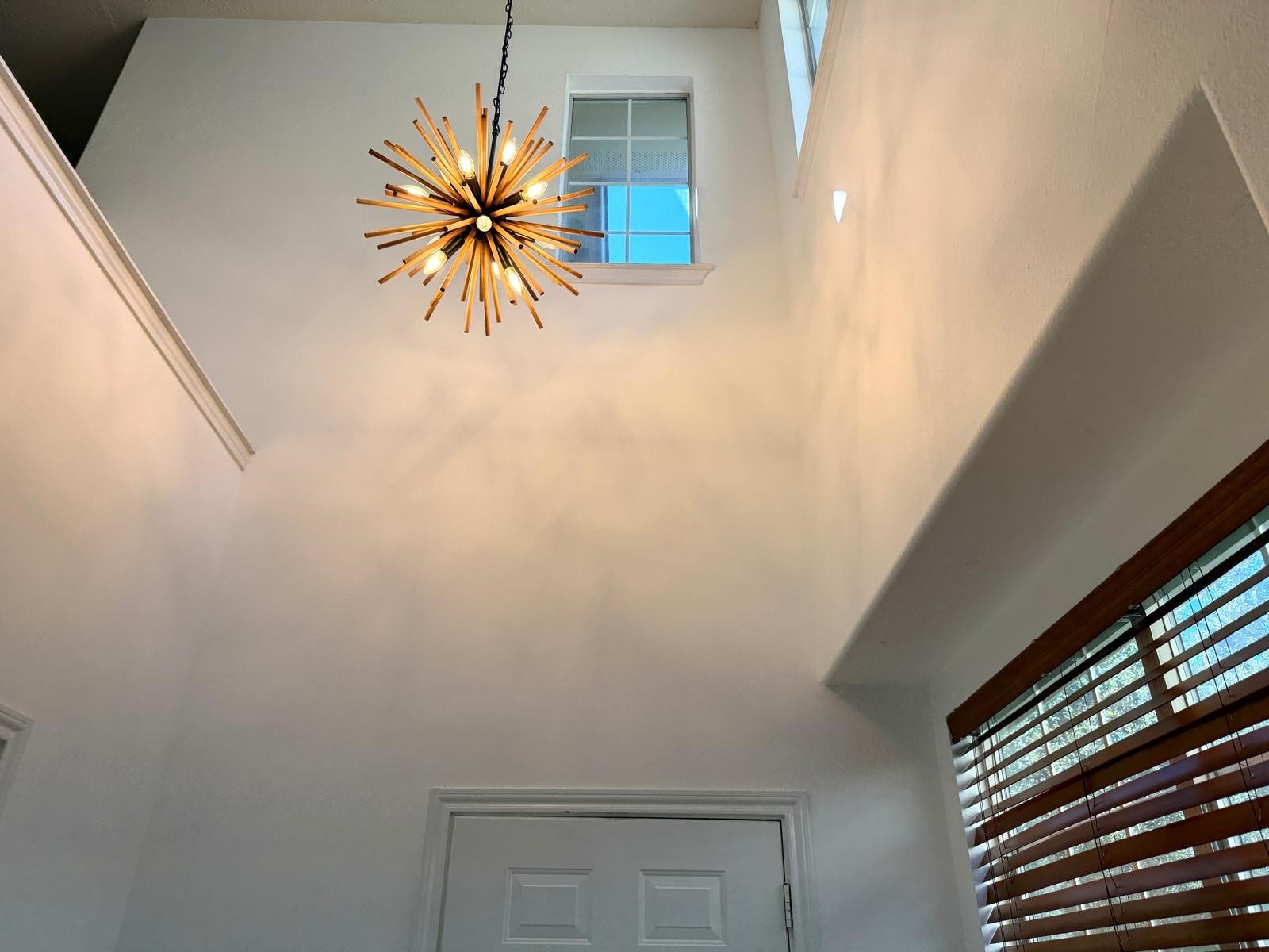 58 S Burberry Park Circle, The Woodlands, TX 77382 Bright and airy entryway featuring a stunning modern chandelier and high ceiling, complemented by natural light streaming through a high window and stylish wooden blinds.