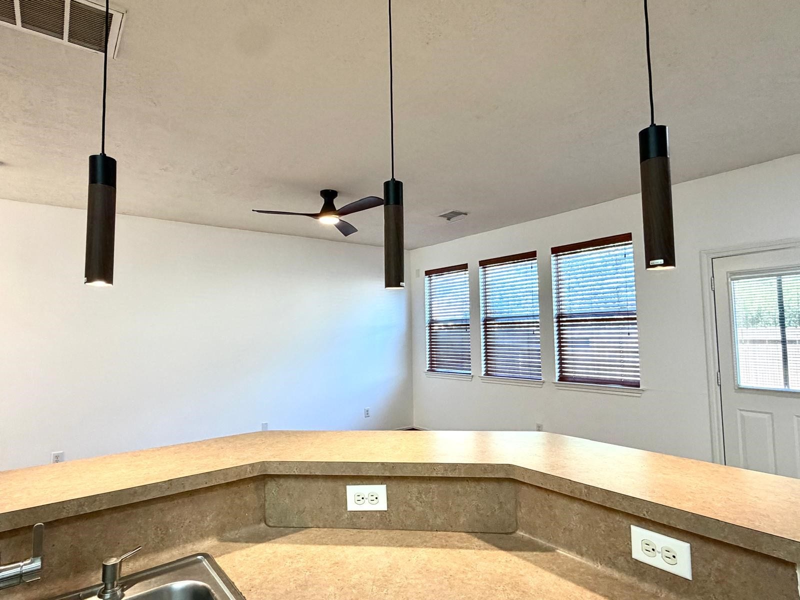 58 S Burberry Park Circle, The Woodlands, TX 77382 Bright and airy living space featuring modern pendant lighting, a ceiling fan, and ample natural light from large windows, complemented by a spacious countertop with a built-in sink.