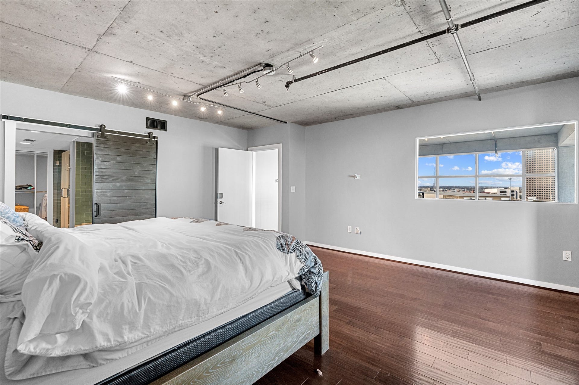 2000 Bagby St Street, #13430, Houston, TX 77002 The primary suite continues the lofts industrial aesthetic with exposed concrete ceilings and warm wood floors, while a wide picture window brings natural light into the private retreat.