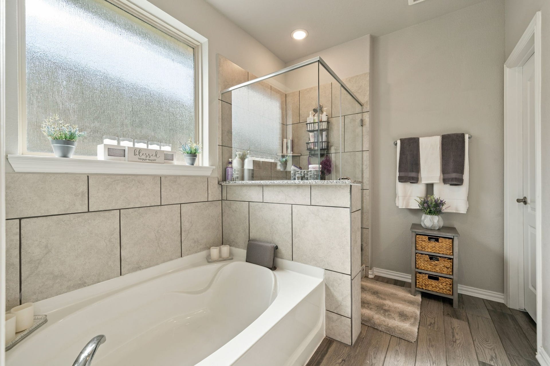 31410 Whitfield Court, Fulshear, TX 77441 Elegant Master bathroom featuring a luxurious soaking tub and a sleek glass-enclosed shower, complemented by stylish tilework and warm wood flooring.