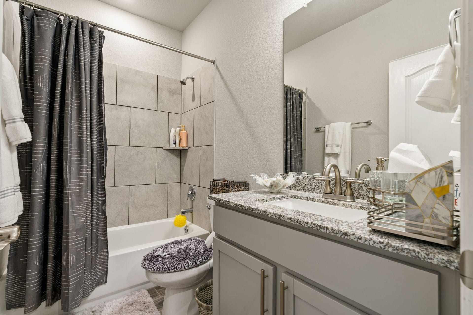 31410 Whitfield Court, Fulshear, TX 77441 Modern bathroom featuring a sleek granite countertop, stylish gray cabinetry, and a tiled shower with a contemporary curtain.