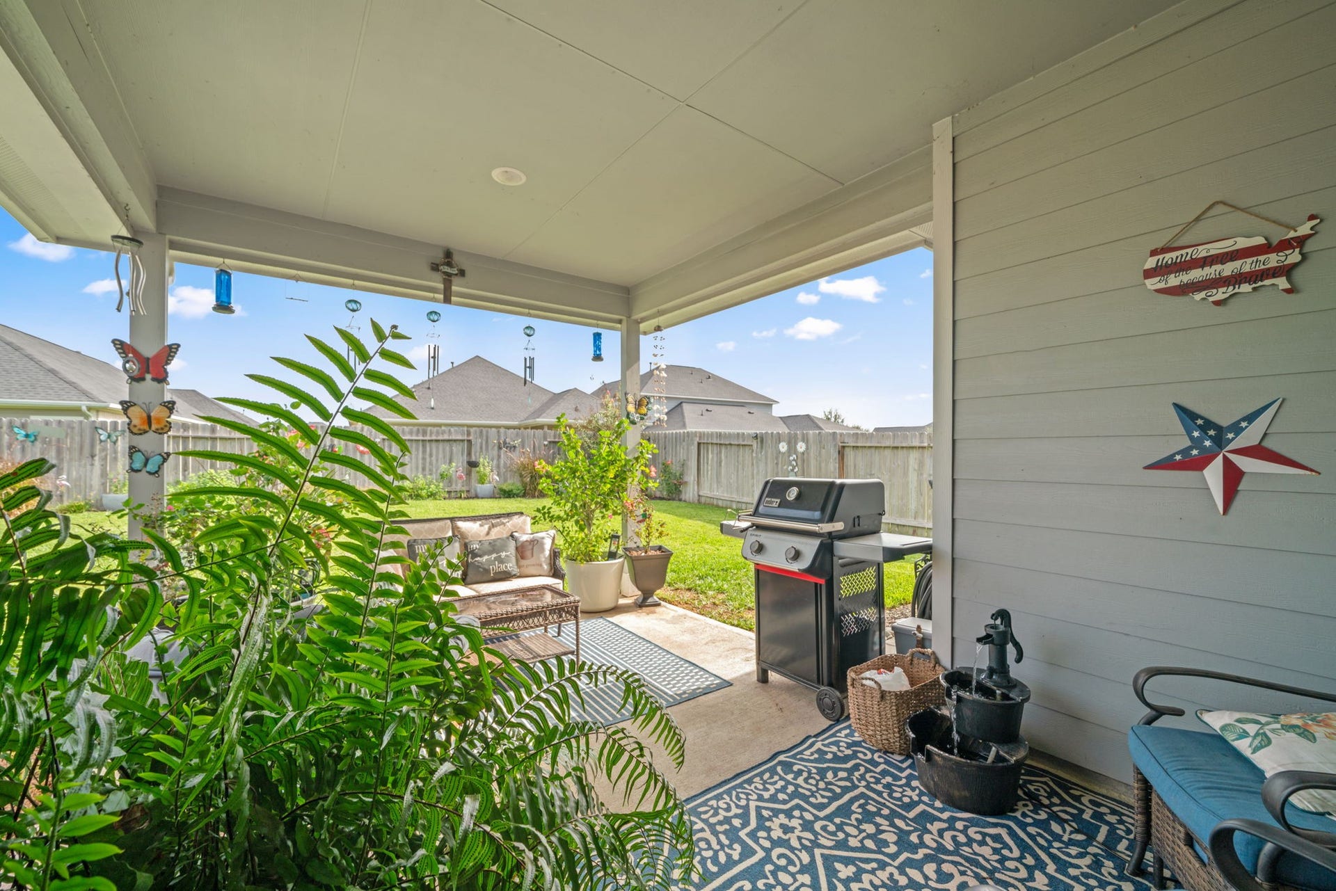 31410 Whitfield Court, Fulshear, TX 77441 Charming covered patio with cozy seating, lush plants, and a barbecue grill, perfect for relaxing and entertaining in a private fenced backyard.