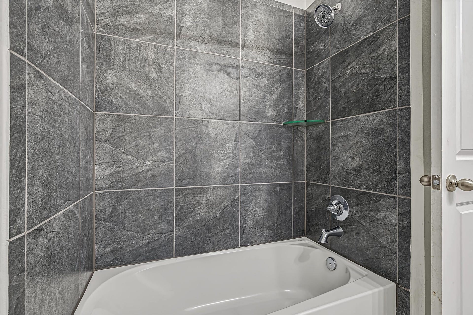9607 Bright Song Lane, Houston, TX 77078 Elegant 2nd bathroom featuring a luxurious bathtub with modern fixtures, surrounded by sleek, dark gray tile walls for a contemporary feel.